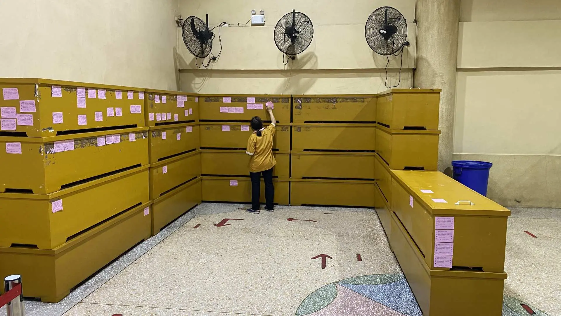 Neatly stacked coffin boxes in the Ruamkatanyu Foundation warehouse in Bangkok, with a volunteer attaching donor merit slips, completing the proxy coffin donation.
