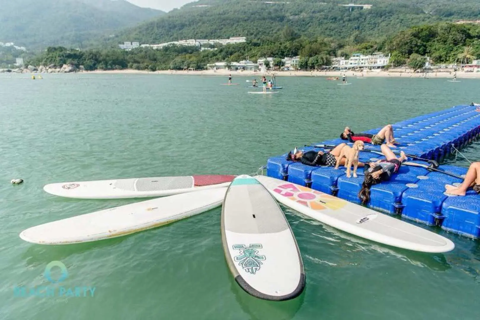 Ván chèo đứng nổi gần một sàn nổi màu xanh tại Long Coast Seasports, Đảo Lantau, với du khách thư giãn và tận hưởng các hoạt động dưới nước nhẹ nhàng tại bãi biển Cheung Sha.