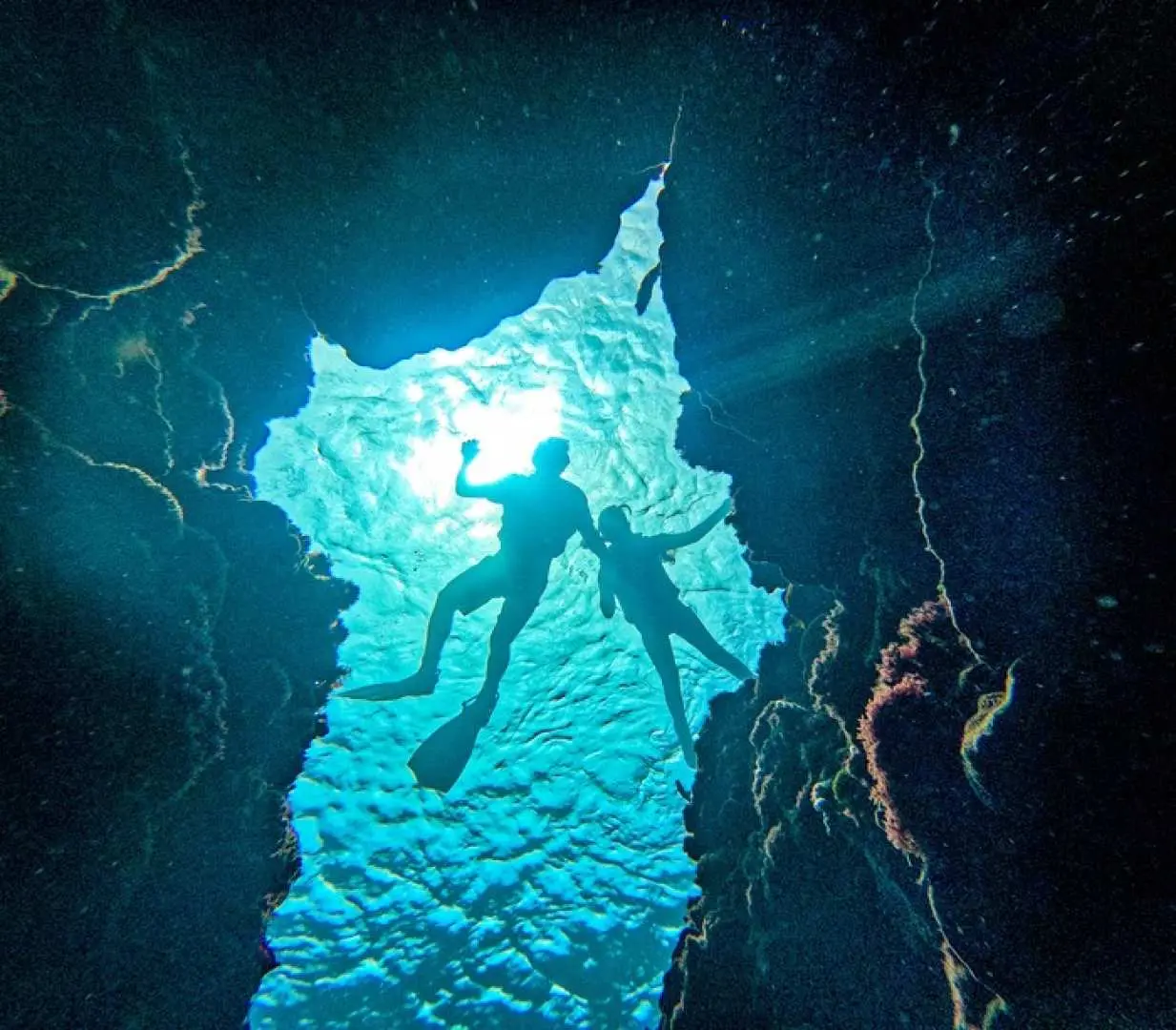 Kenting Houbihu snorkeling: visitors in a unique rock crevice or underwater cave look up at the bright blue light and surface ripples, experiencing a distinctive underwater adventure perspective.