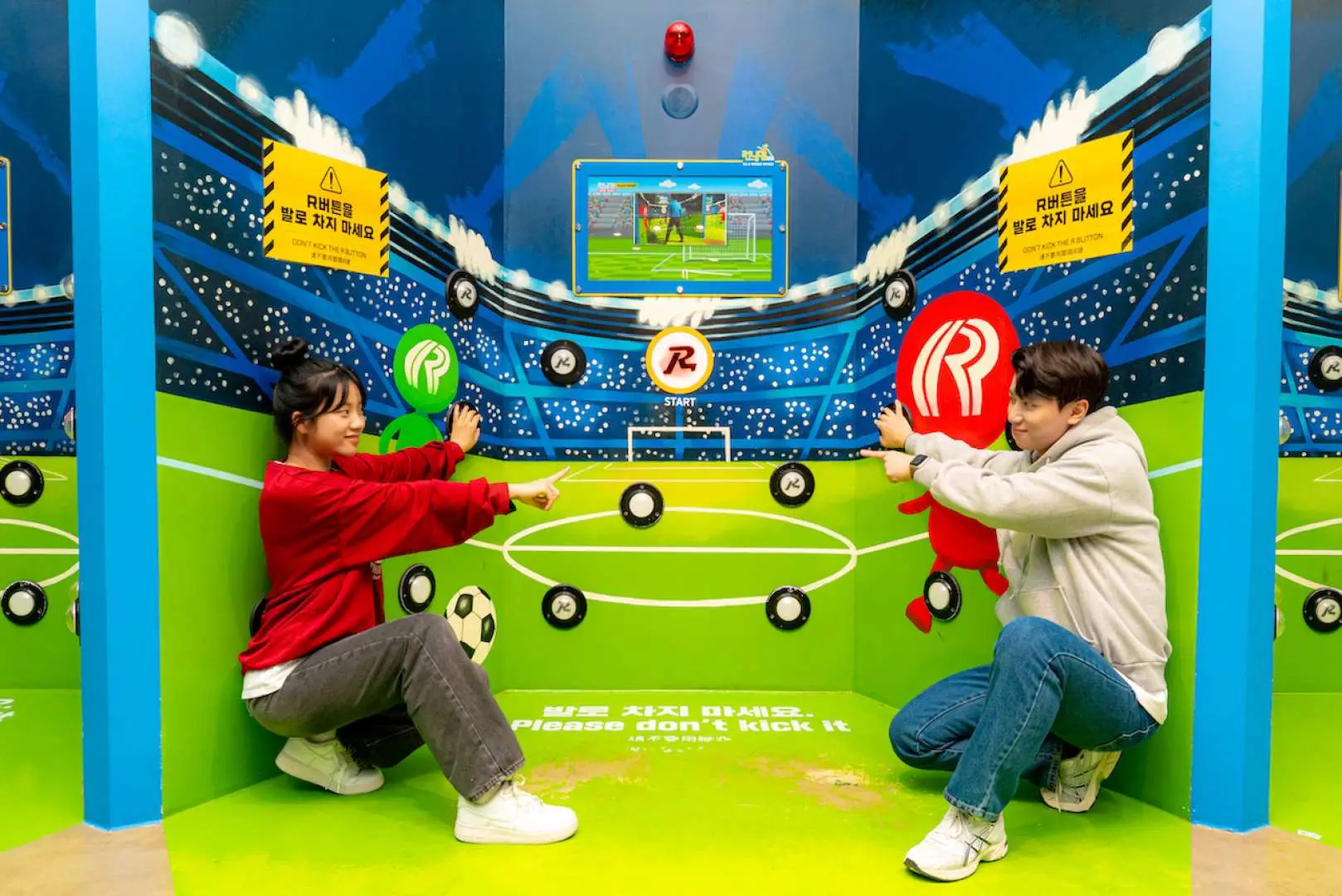 Two visitors engage in an interactive soccer-themed game at Busan Running Man Experience Center's football mission zone, completing challenges.