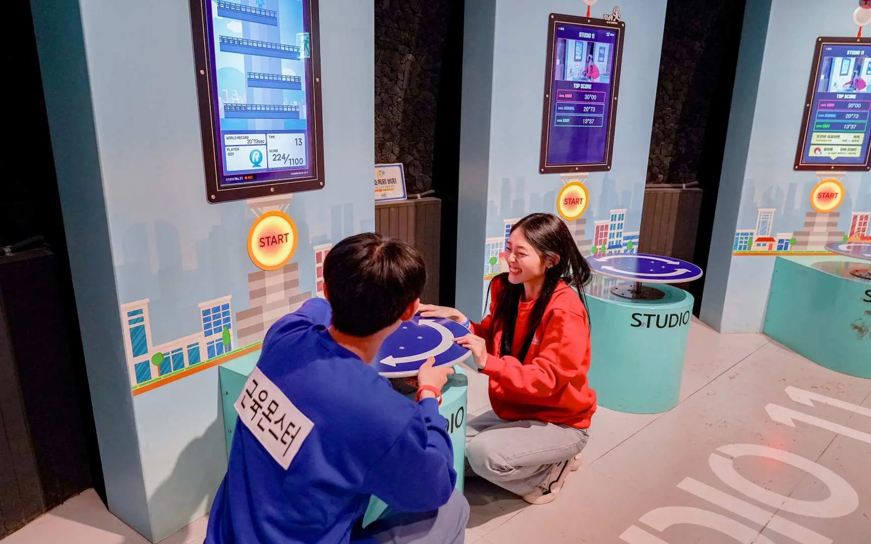 At Gangneung Running Man Experience Center's 'Studio 11', two players happily engage in an interactive desktop R-mon themed bingo mission, enjoying the game.