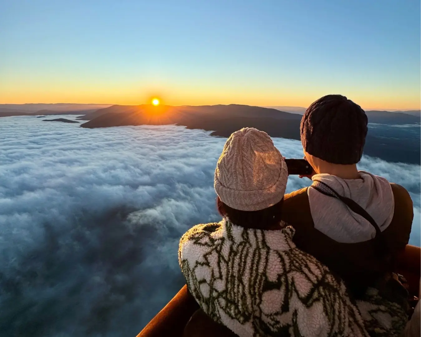 两位旅客从澳大利亚亚拉河谷的热气球上俯瞰壮观的云海日出，金色的光芒染红天际，体验令人屏息的维多利亚州高空美景。
