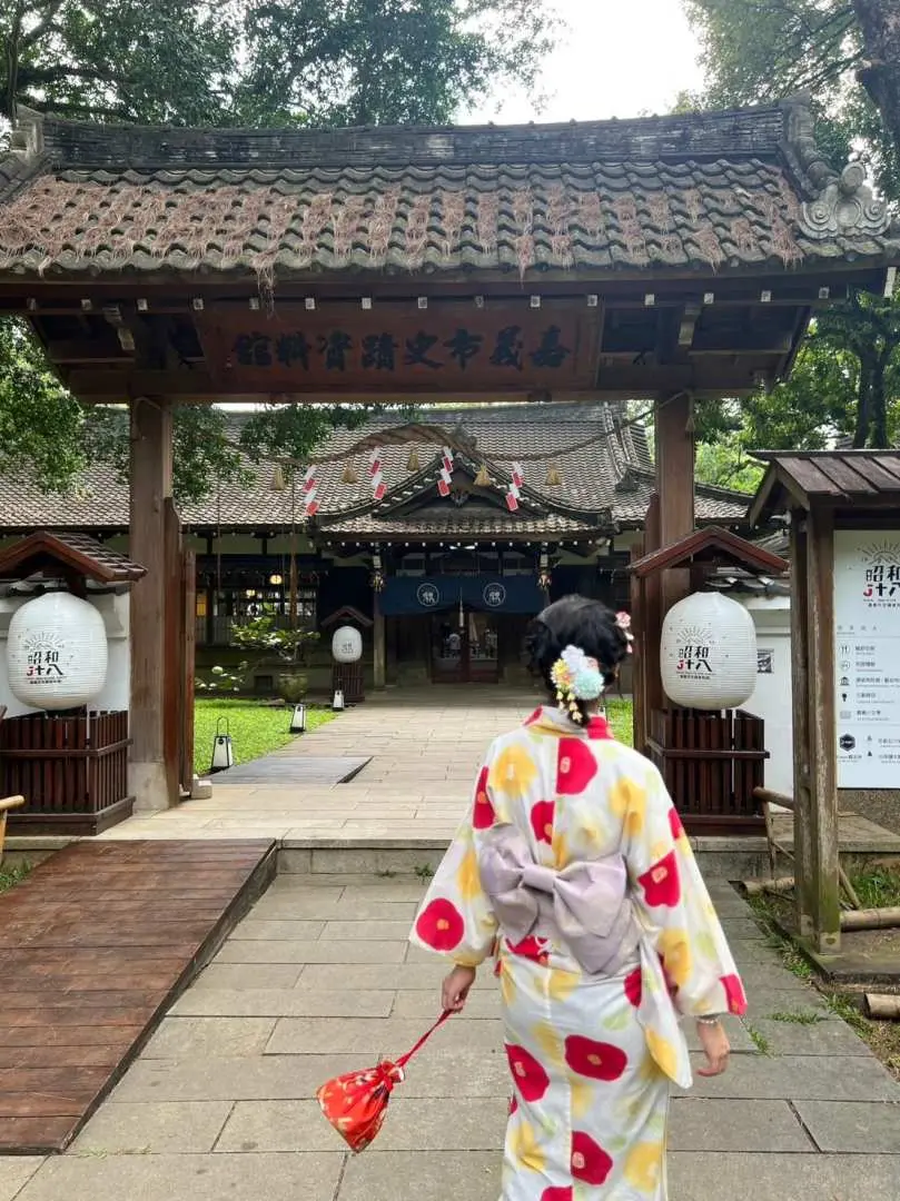 一位身著和服的女性手持紙扇，漫步於嘉義昭和十八J18-史蹟資料館的日式鳥居前，體驗文化與美拍的網美必拍景點。