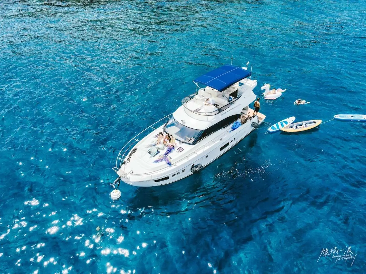 Aerial view of Fangxing luxury yacht anchored in clear turquoise waters near Xiaoliuqiu, Pingtung, Taiwan, with guests enjoying various water activities like kayaking and SUP under a blue sky.