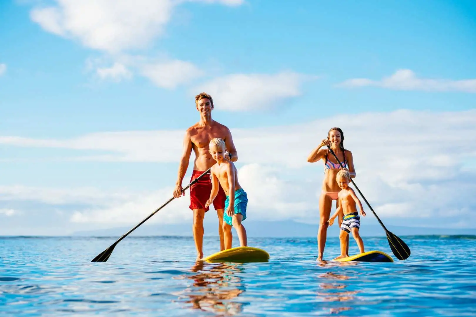 A family enjoying stand-up paddleboarding in Miami's clear waters under a sunny blue sky, an ideal water activity to experience with the Explorer Pass.