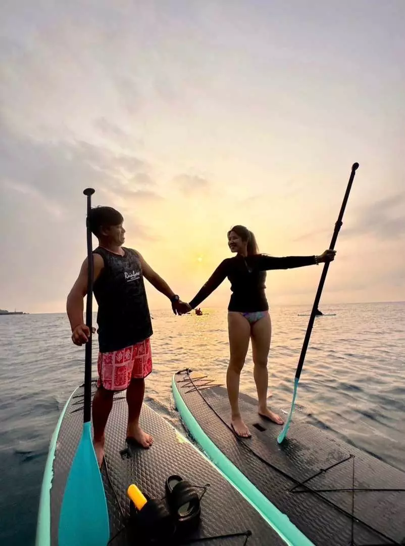 小琉球夕陽餘暉中，一對情侶手牽手站在各自的立槳衝浪板上，享受浪漫的海上漂浮時光，捕捉與教練協助拍攝的難忘美照。
