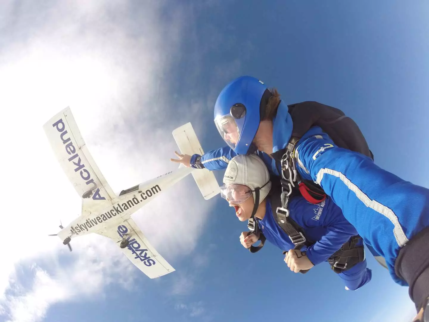 Tandem skydivers in Auckland just after exiting the plane, thousands of feet above, gazing down at the New Zealand landscape, capturing the thrilling moment of freefall.