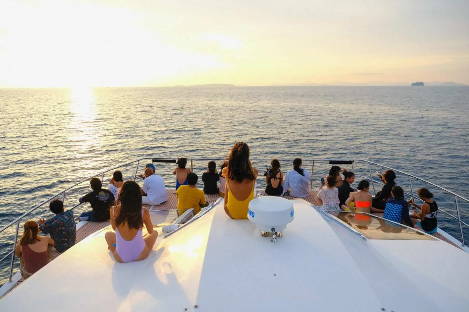 Travelers sitting on the deck of a luxury catamaran, enjoying the magnificent sunset sea view during the Phi Phi and Bamboo Island sunset tour in Thailand.