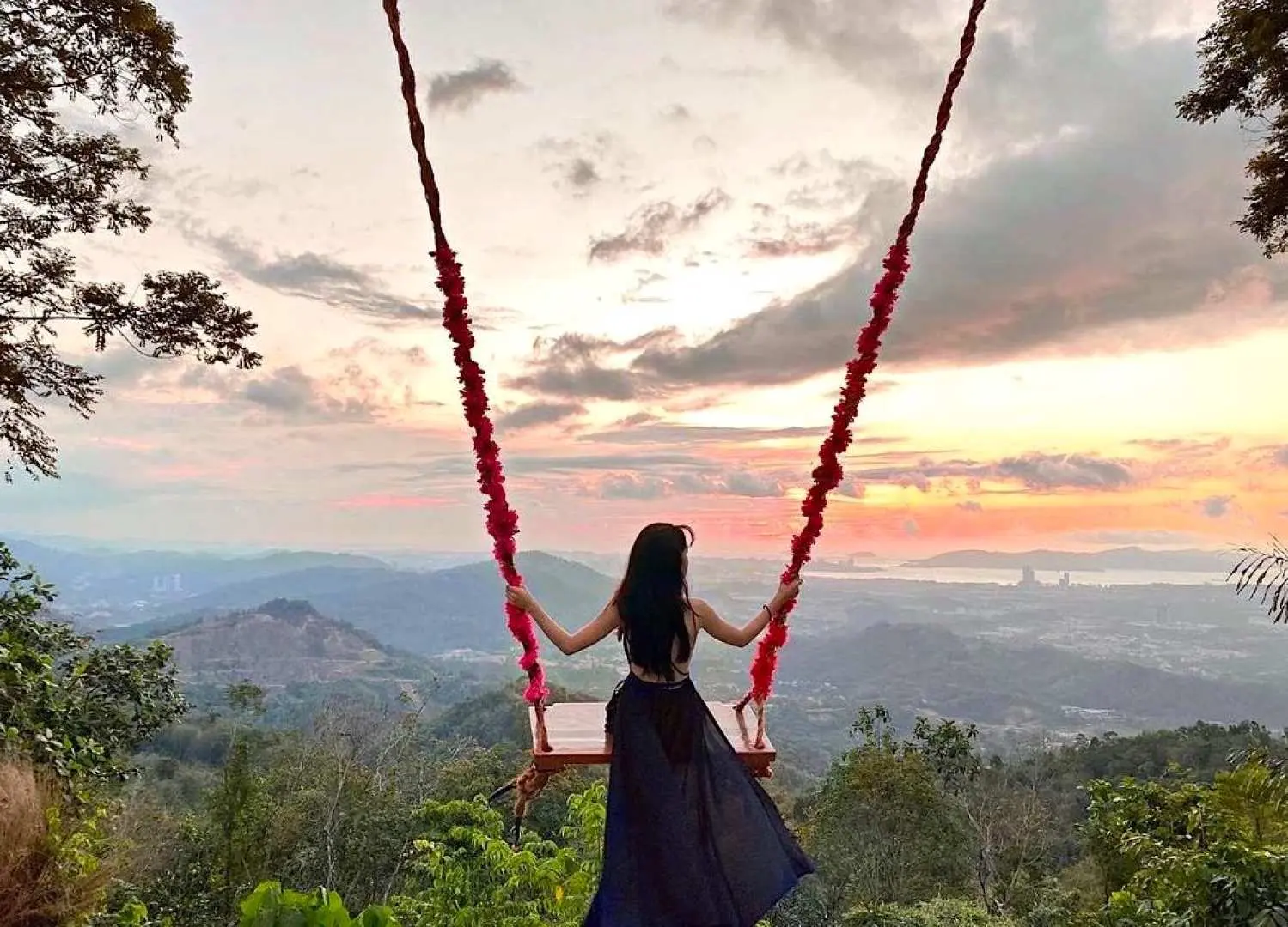 Woman on Kokol Hill Elf's scenic swing, back to the sunset and mountain views, enjoying a romantic moment during the Kota Kinabalu half-day tour.