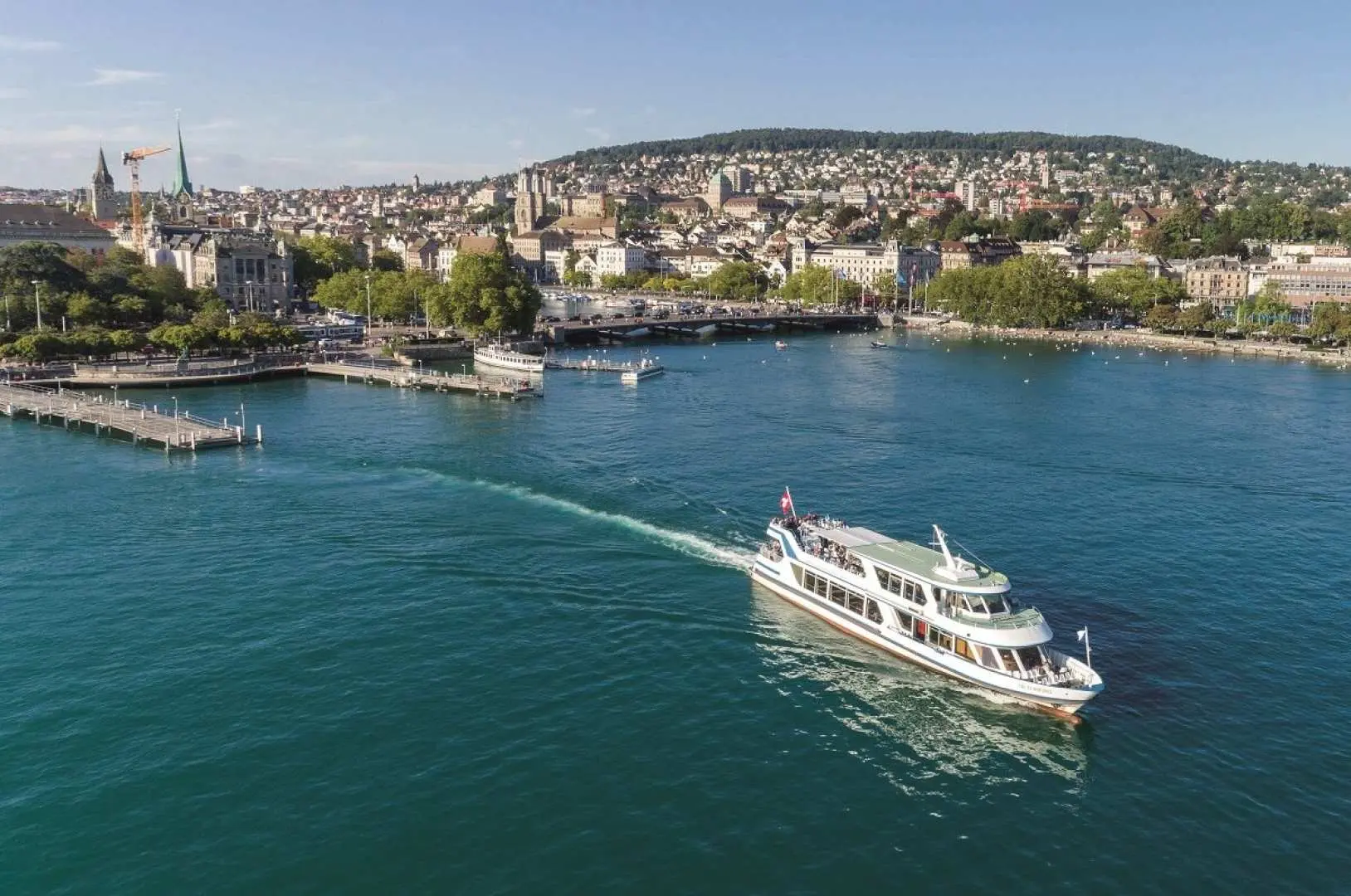 Zurich Lake cruise experience, a double-decker boat sailing on the azure lake with the Zurich city skyline and distant mountains in the background, offering visitors a unique perspective of Switzerland's lake and mountain scenery.