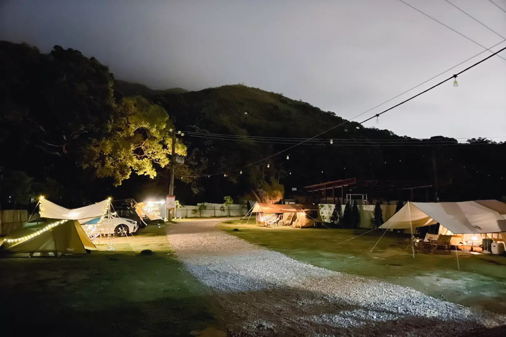 香港红花岭Autocamper豪华露营区的夜间全景，多个Ogawa Type52R帐篷与汽车沿着碎石路排开，点点灯光营造温馨热闹的夜晚氛围。