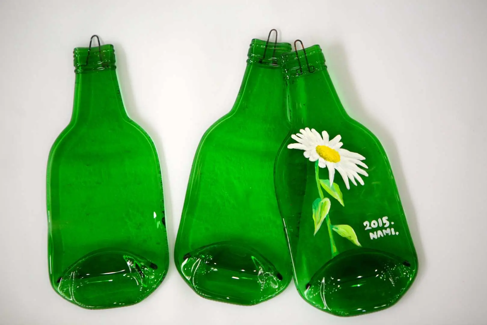 南怡島燒酒瓶彩繪體驗的創意作品，三片扁平綠色玻璃瓶，其中一片繪有白色雛菊圖案。