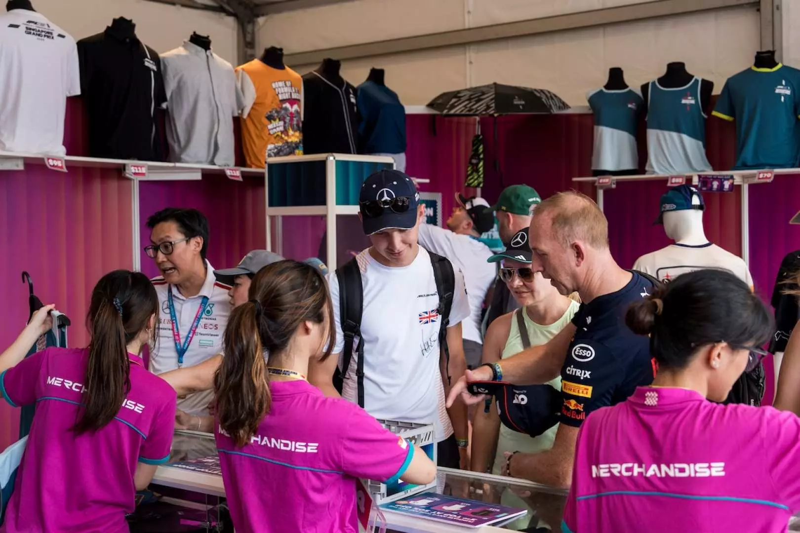 Fans browsing and purchasing exclusive F1 merchandise, apparel, and souvenirs at a bustling official stall during the 2026 F1 Singapore Grand Prix.
