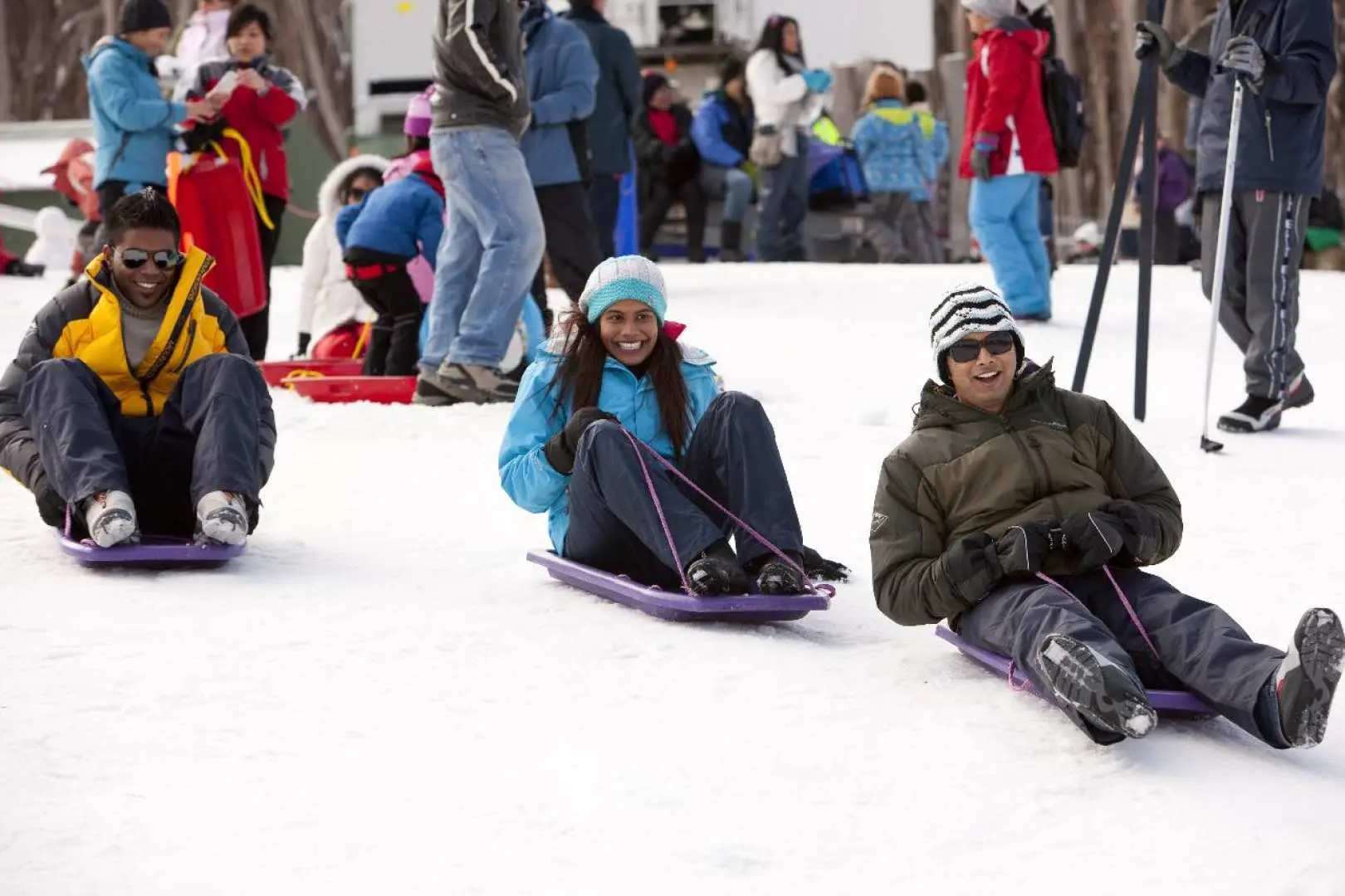Young people gleefully toboggan down a gentle snowy slope at Lake Mountain, enjoying exhilarating snow play and winter fun on this memorable Melbourne day trip.