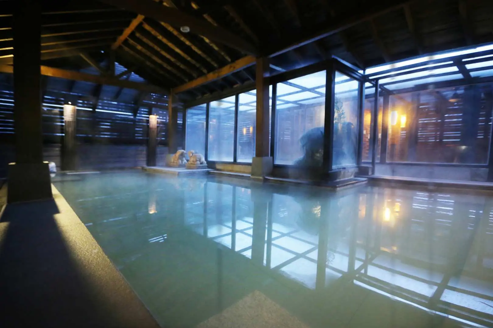 Beitou Shanshui Le Lodge's spacious public indoor hot spring bath, featuring a steamy pool, wooden ceiling, and large windows that create a serene, nostalgic yet modern bathing atmosphere.