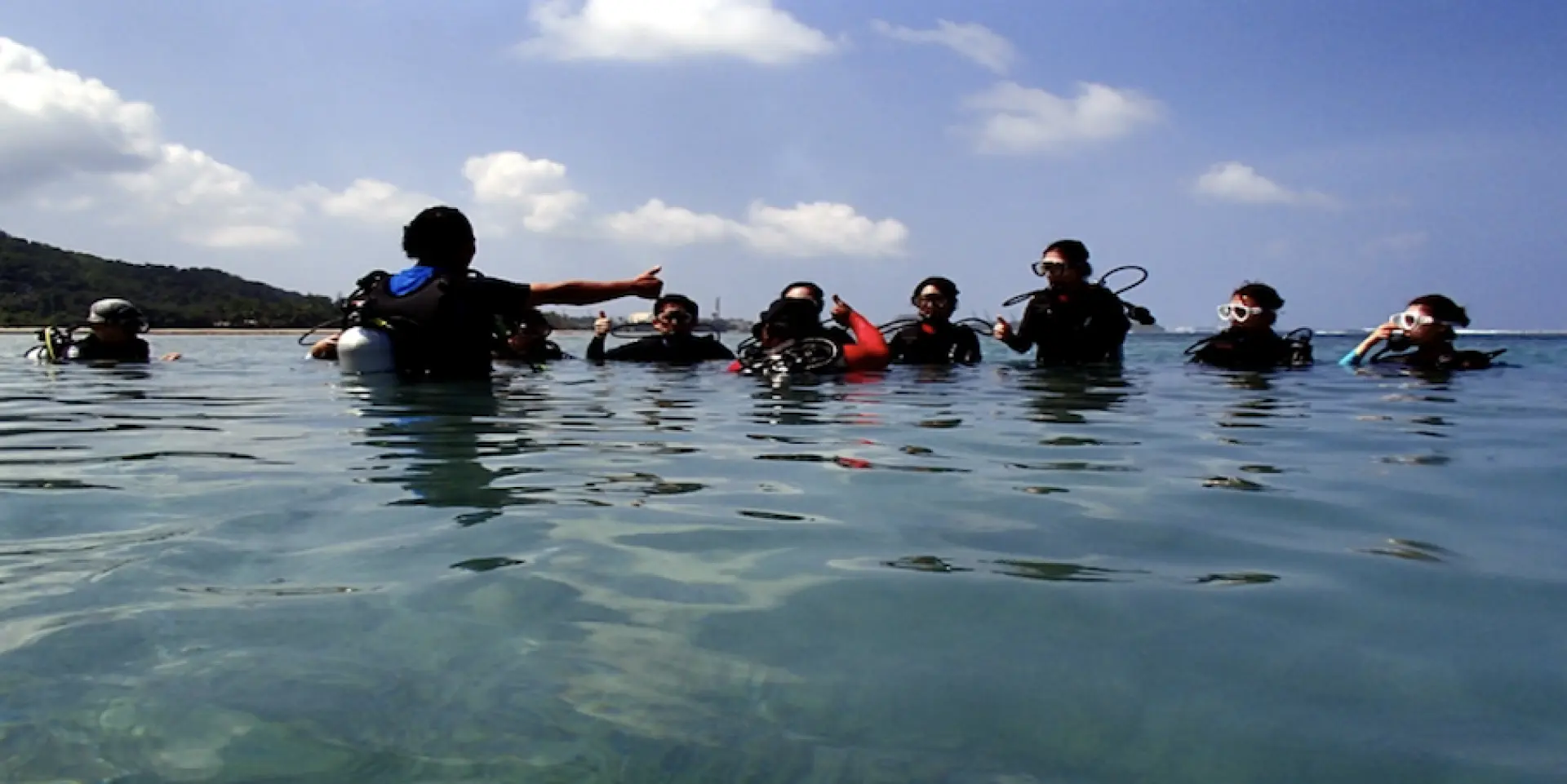 A group of enthusiastic participants in Guam's clear ocean receiving instructions from a Korean instructor, preparing for their guided introductory dive at Fish Eye Point.