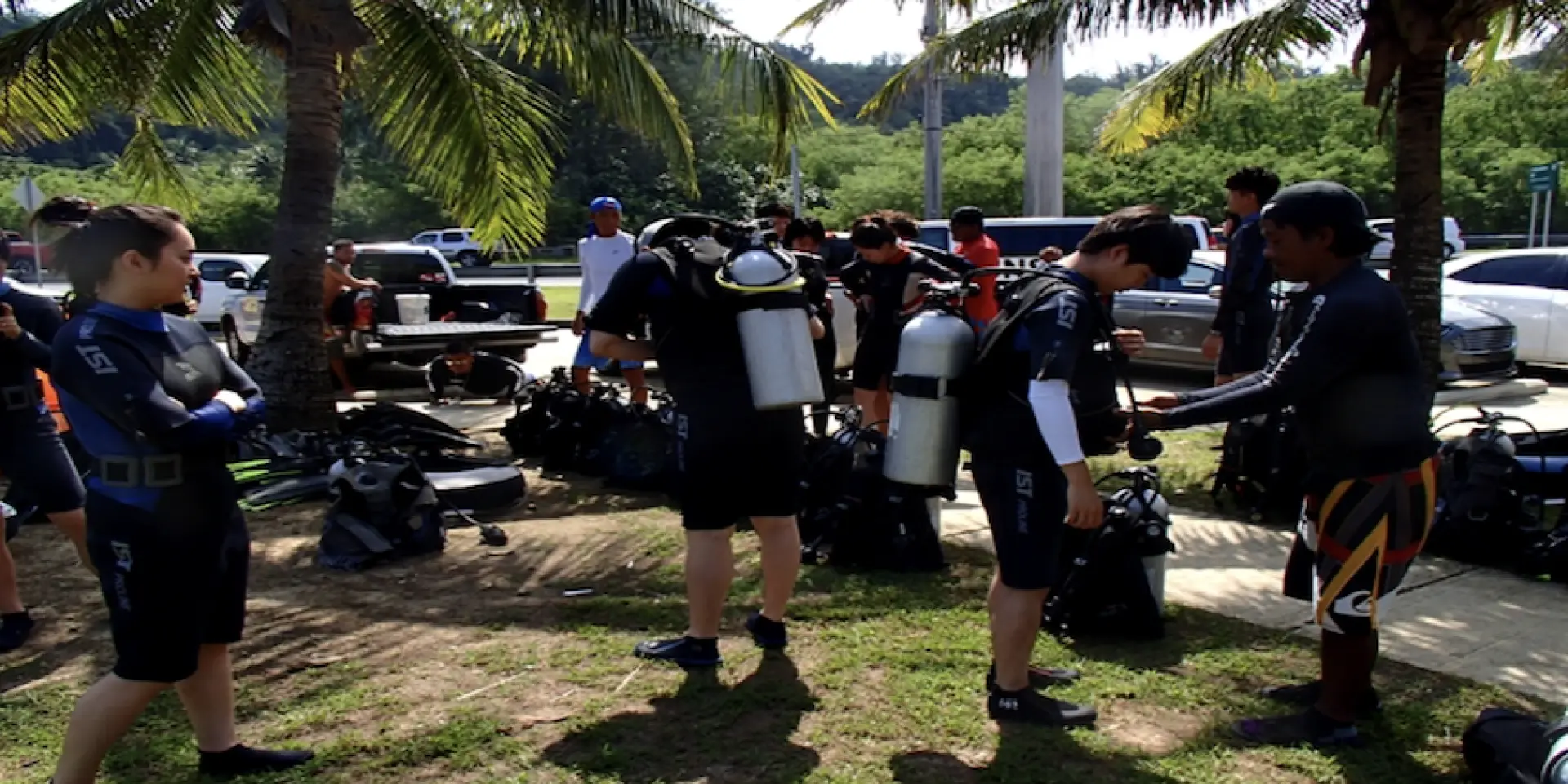 Divers preparing and getting their scuba gear fitted with assistance on land in Guam, highlighting the comprehensive support for the introductory diving experience.