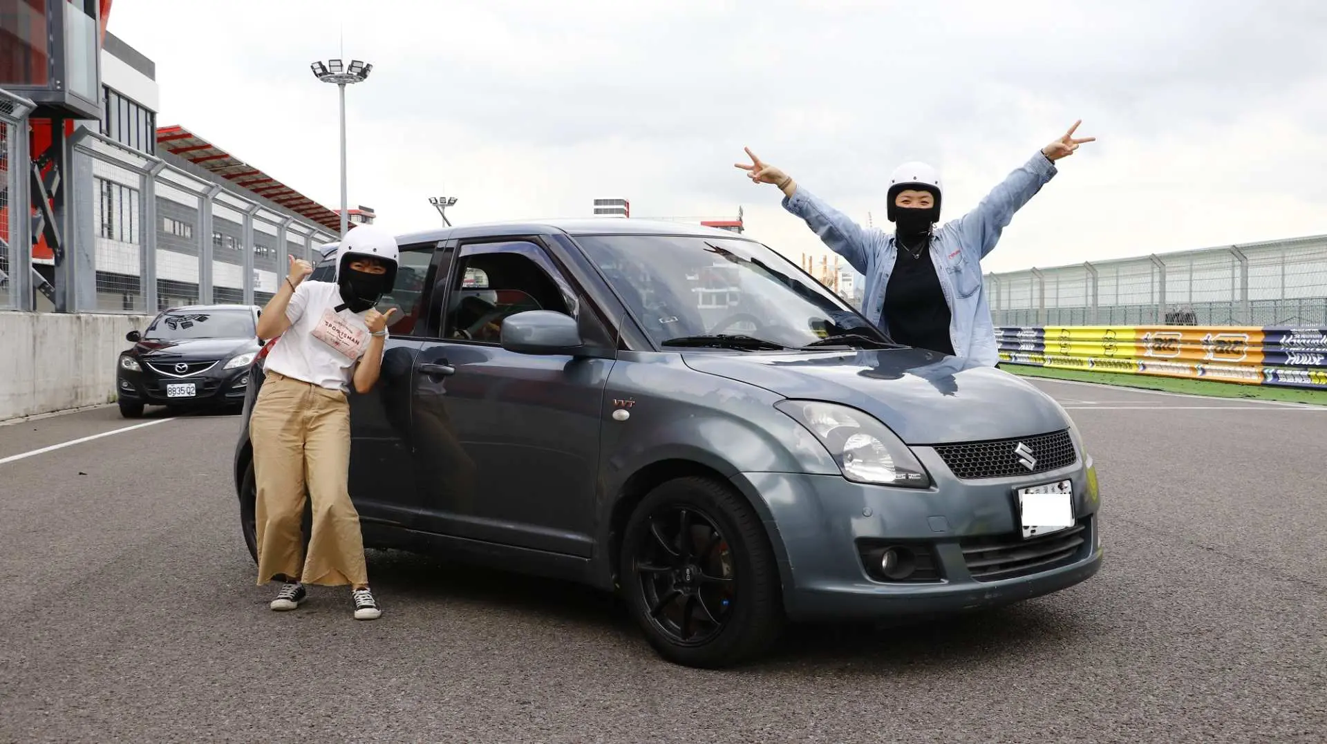 兩位戴著頭盔的學員在麗寶國際賽車場上，興奮地與自駕車輛合照，準備享受賽道體驗。