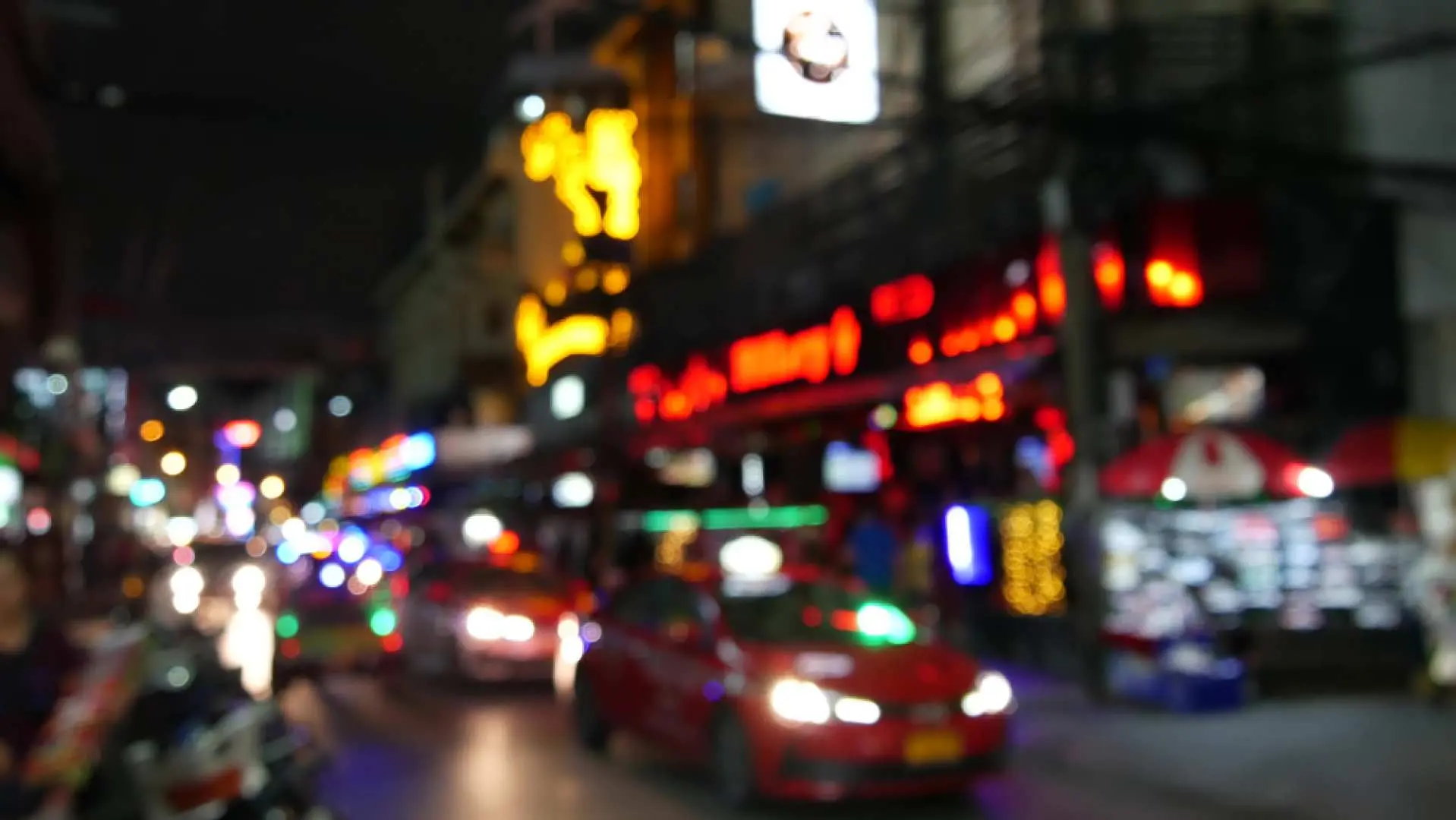 Blurred lights of Bangkok's night streets, with cars and neon signs creating a dynamic glow, capturing the vibrant atmosphere during a bar hopping tour.