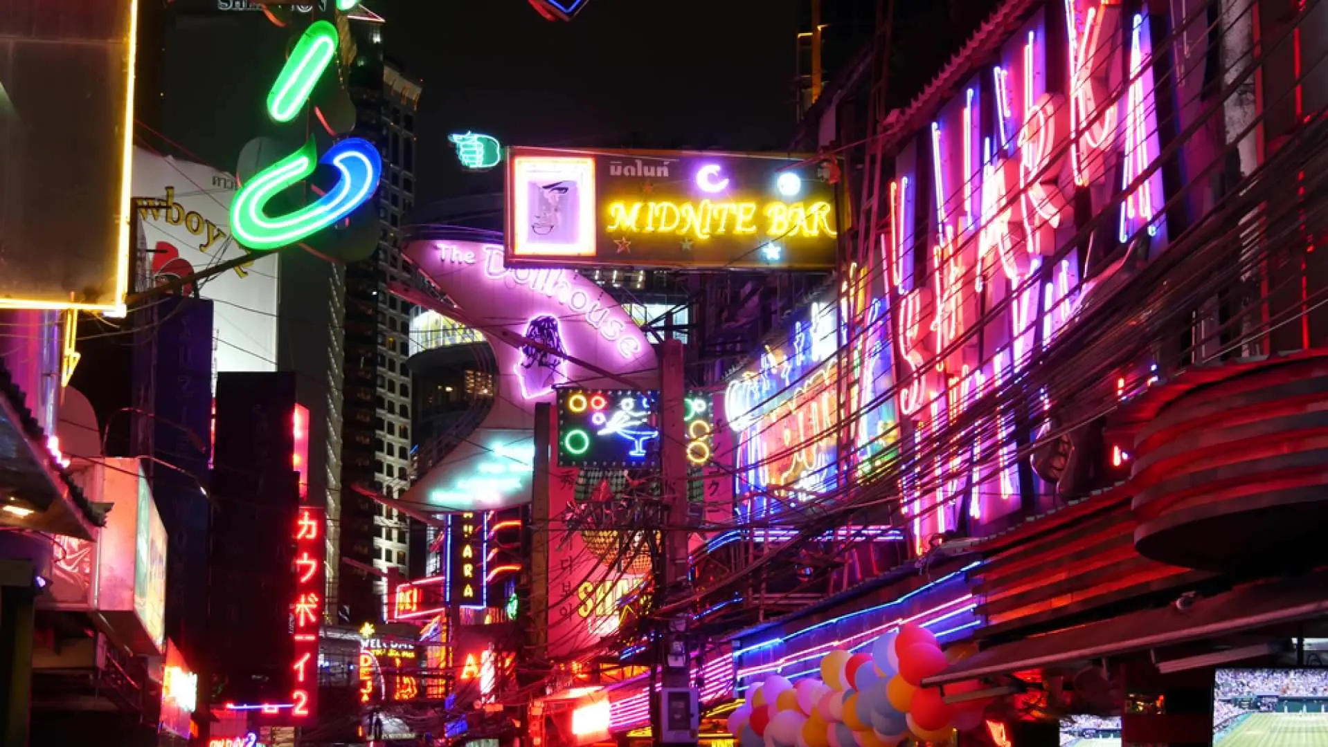 Bustling nightlife scene in Bangkok's Soi Cowboy, with vibrant neon bar signs illuminating the street, showcasing the lively atmosphere of a guided bar hopping tour.