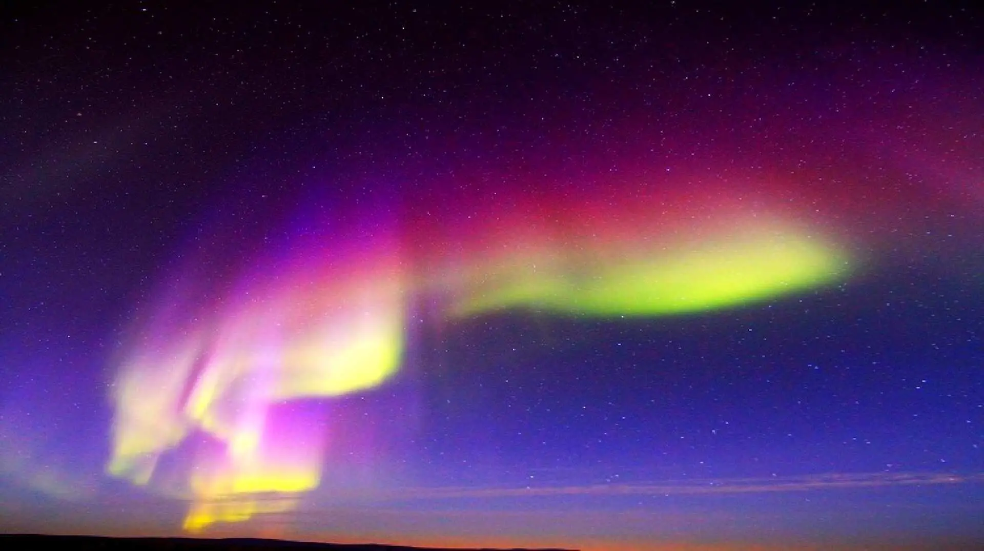 Multicolor aurora display with purple, green, yellow, and red hues blending in the Fairbanks night sky, offering a magical and diverse viewing experience from a remote cabin.