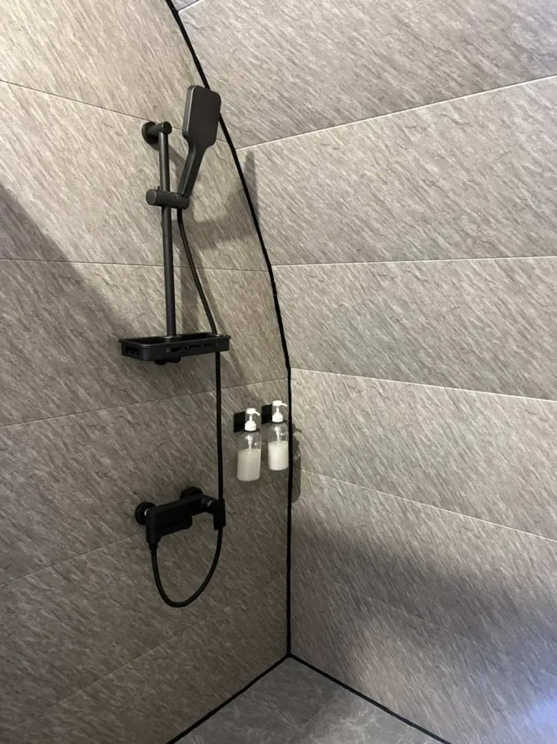 Modern bathroom inside a Meishanqing Glamping luxury ark cabin, with a stylish black shower head and faucet on grey tiled walls, offering a clean and comfortable space.