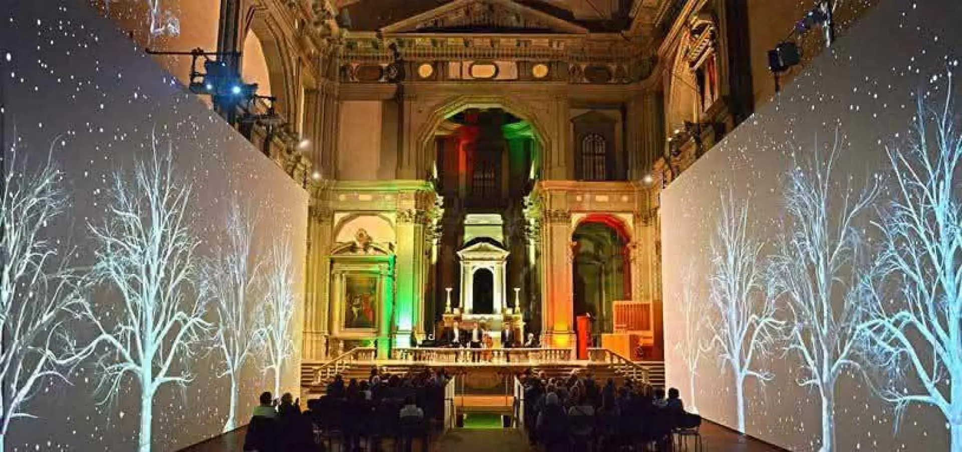 Audience enjoys a classic opera music dinner inside Florence's St. Stephen's Church, featuring enchanting winter tree projections on the walls.