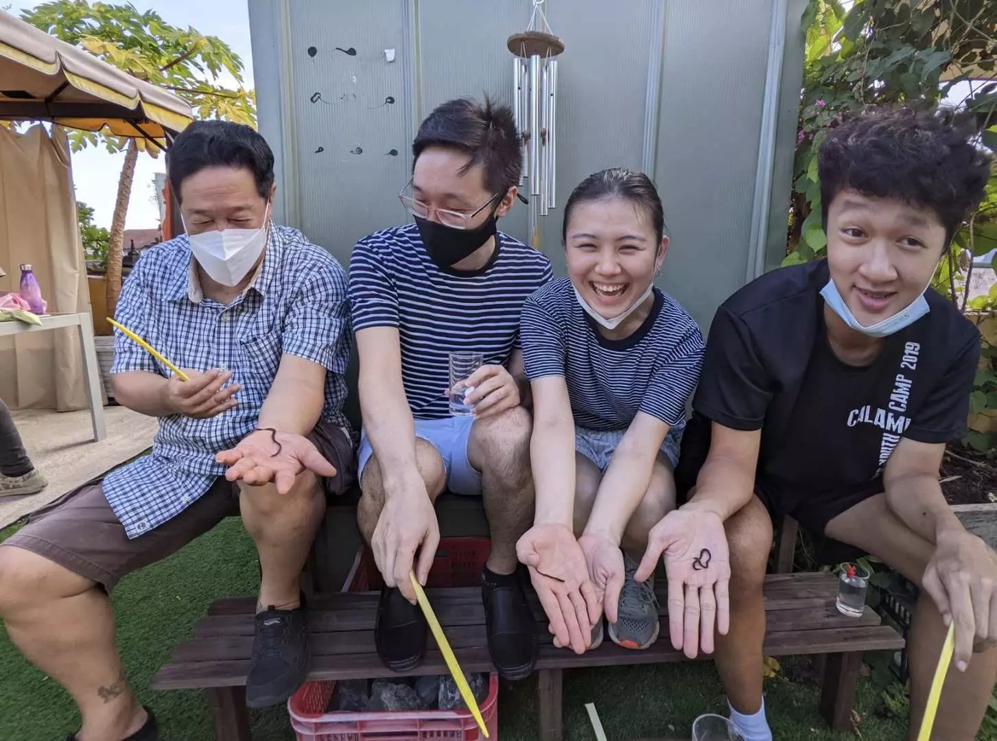 シンガポールSundowner農場での家族向け体験。屋外のベンチに座った訪問者が、手にしたミミズを嬉しそうに見せ、自然を満喫する様子。