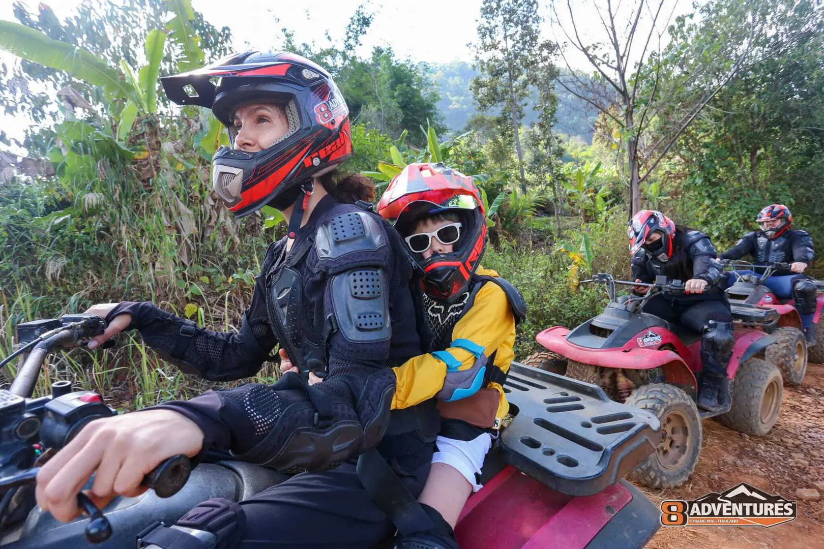Chuyến đi xe địa hình ATV ở Chiang Mai, Thái Lan, một người lớn và một trẻ em đội mũ bảo hiểm và đồ bảo hộ, cùng nhau vui vẻ lái xe ATV màu đỏ, tận hưởng niềm vui phiêu lưu cùng gia đình.