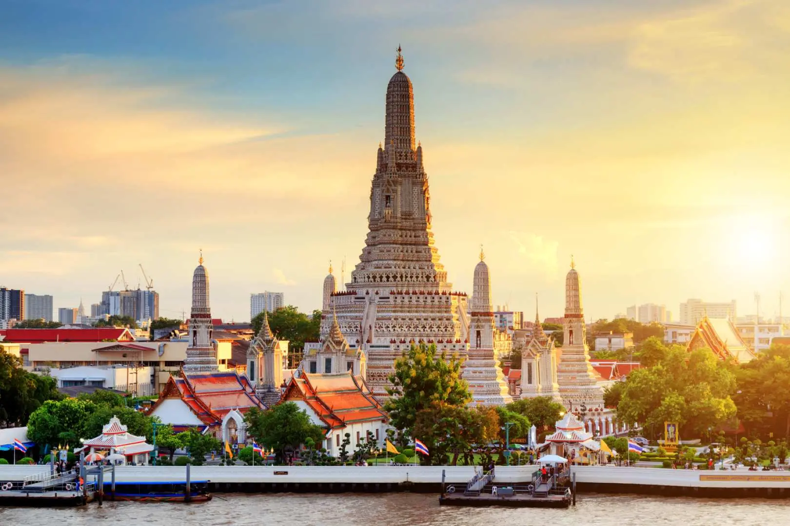 The majestic Wat Arun (Temple of Dawn) pagodas stand tall against a golden sunset, reflecting beautifully on the Chao Phraya River, showcasing Bangkok's historical grandeur.