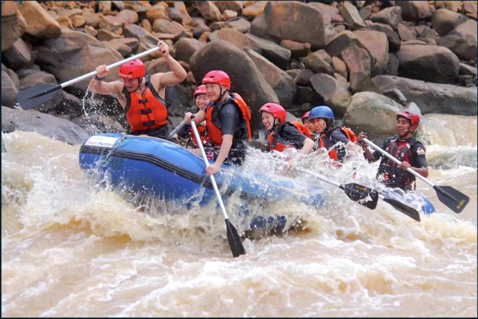 Enthusiastic participants in red safety gear paddle through the challenging Grade 3-4 rapids of Sabah's Padas River, experiencing a thrilling white-water rafting adventure near Kota Kinabalu.
