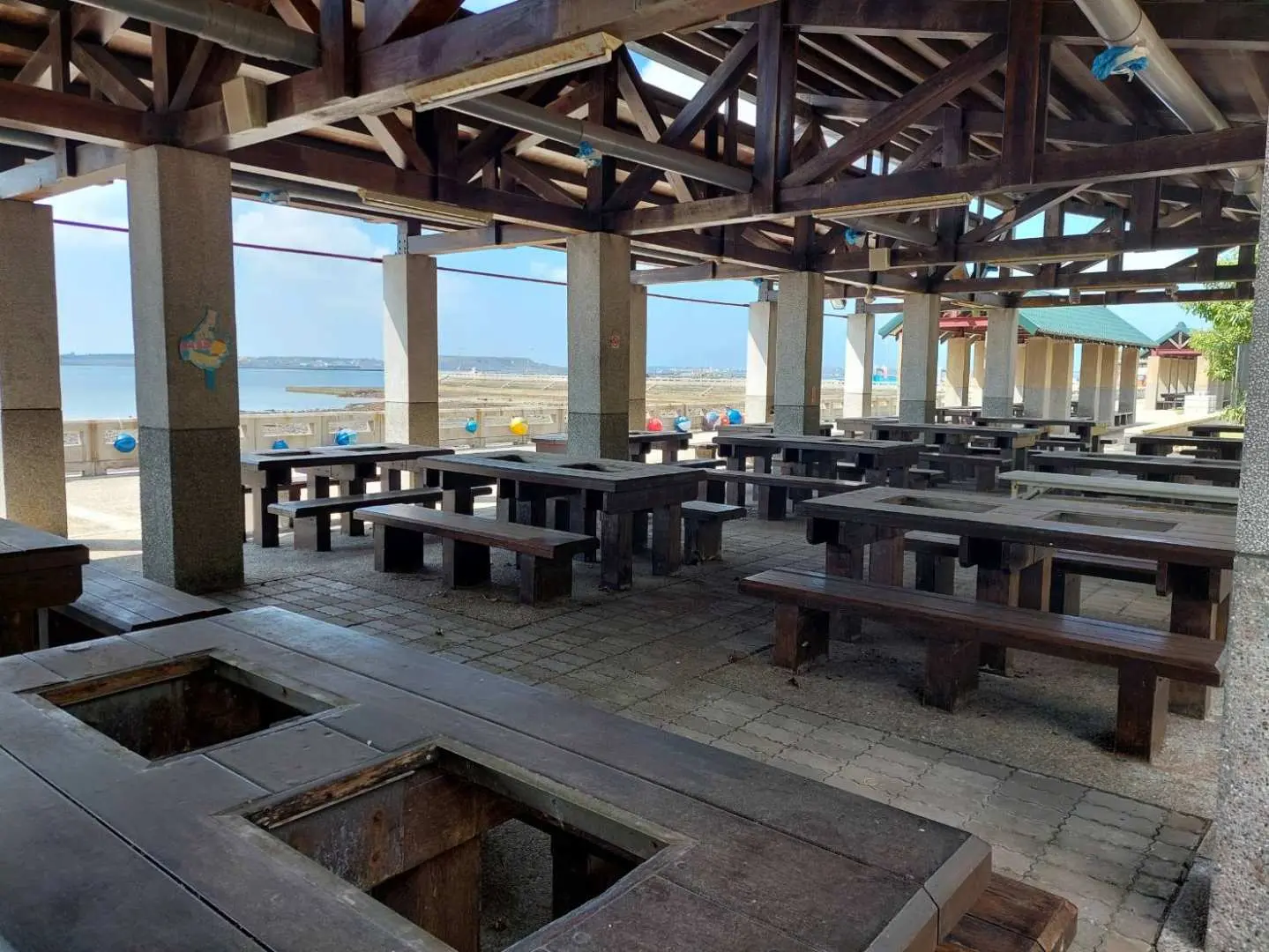 澎湖海洋牧場的寬敞戶外用餐區，設有許多附烤爐的木質餐桌，讓團體遊客能舒適地享受鮮蚵炭烤與海鮮粥，同時欣賞海景。