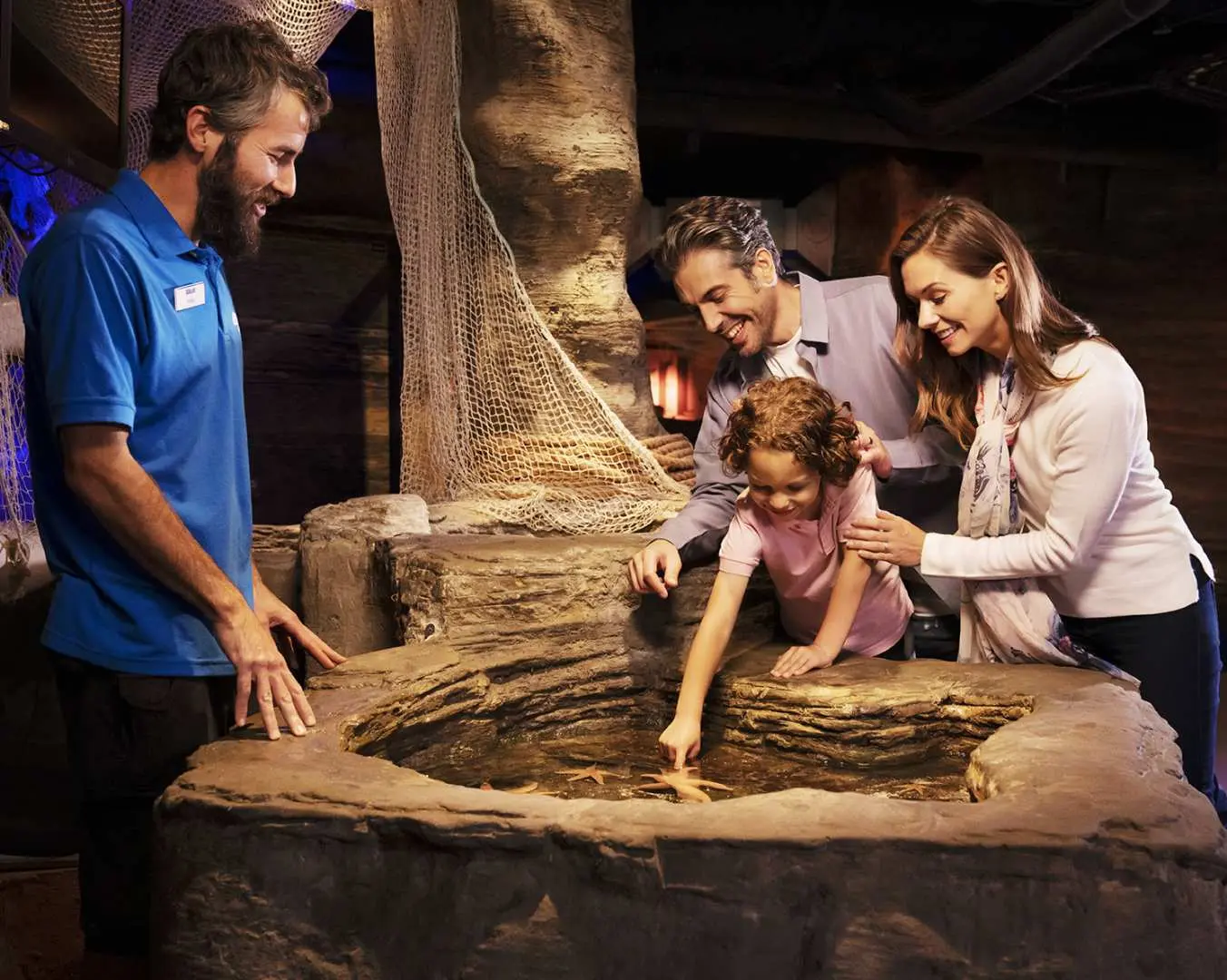 An aquarium staff member enthusiastically introduces marine life to a family of three at the London SEA LIFE Aquarium's interactive touch pool, offering an enriching learning experience in London's underwater world.
