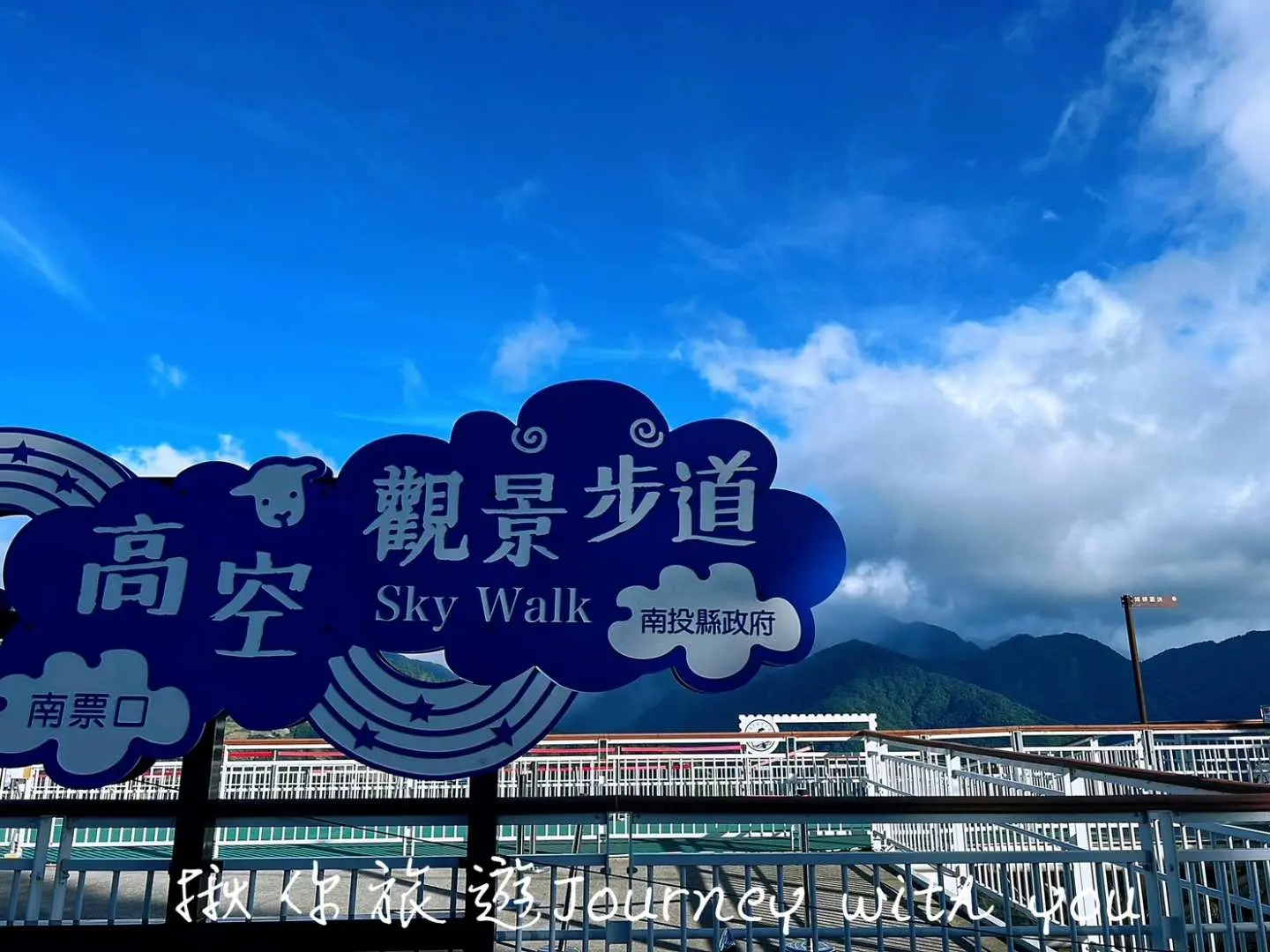 蓝天白云下清境高空步道标志，提醒游客即将踏上南投独特的户外健行体验，远方山脉壮丽景色尽收眼底。