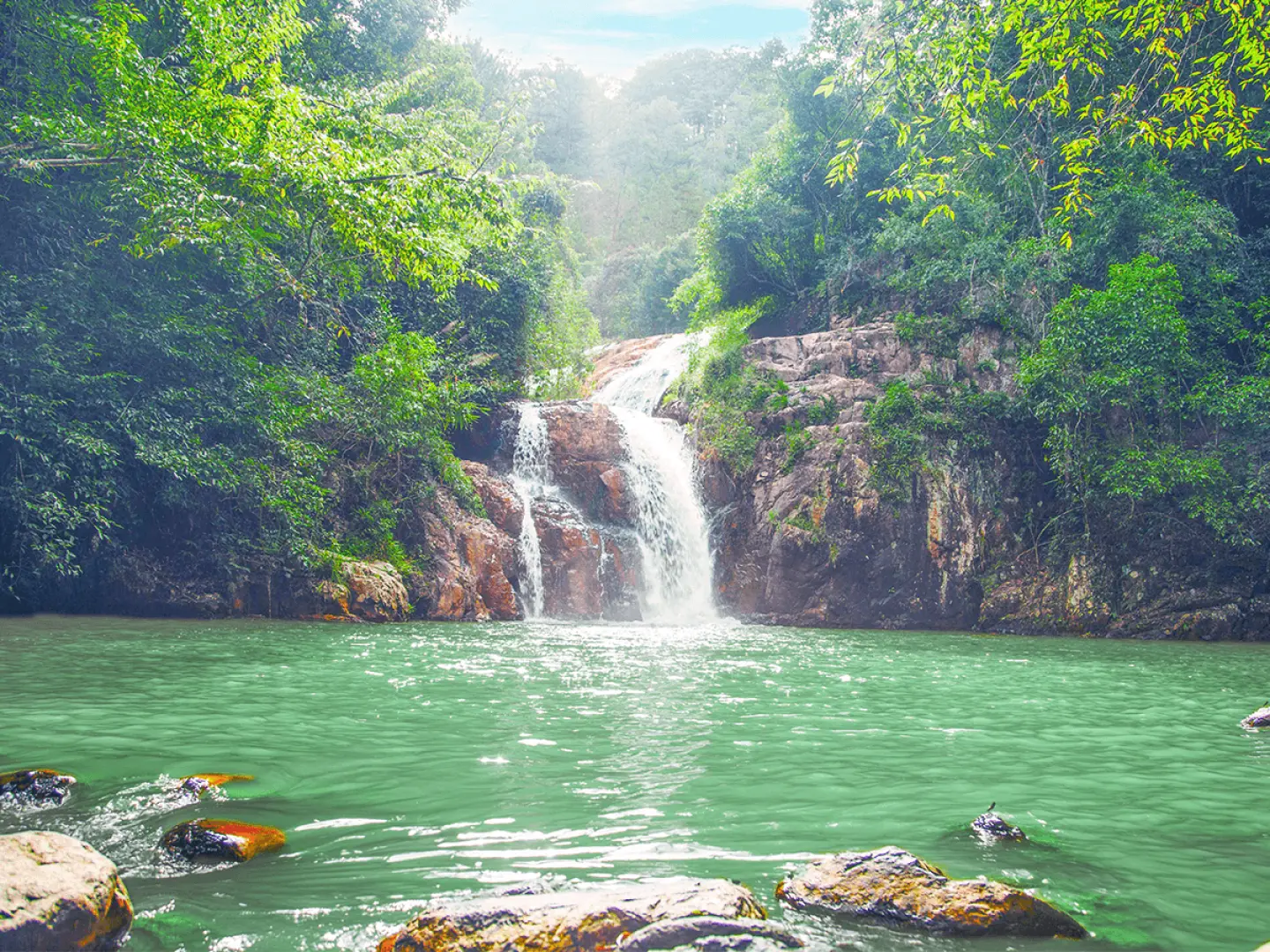 The majestic Datanla Waterfall in Da Lat, featuring multi-tiered cascades flowing into a serene turquoise pool, surrounded by lush tropical forest with sunlight filtering through the trees.