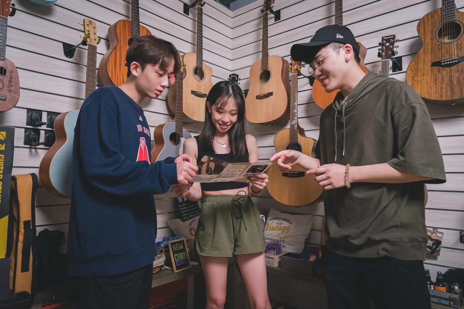 Three participants in a Taipei recording studio, standing in front of a guitar wall, jointly reviewing a newly recorded music piece or discussing MV content, enjoying precious time creating music with friends.