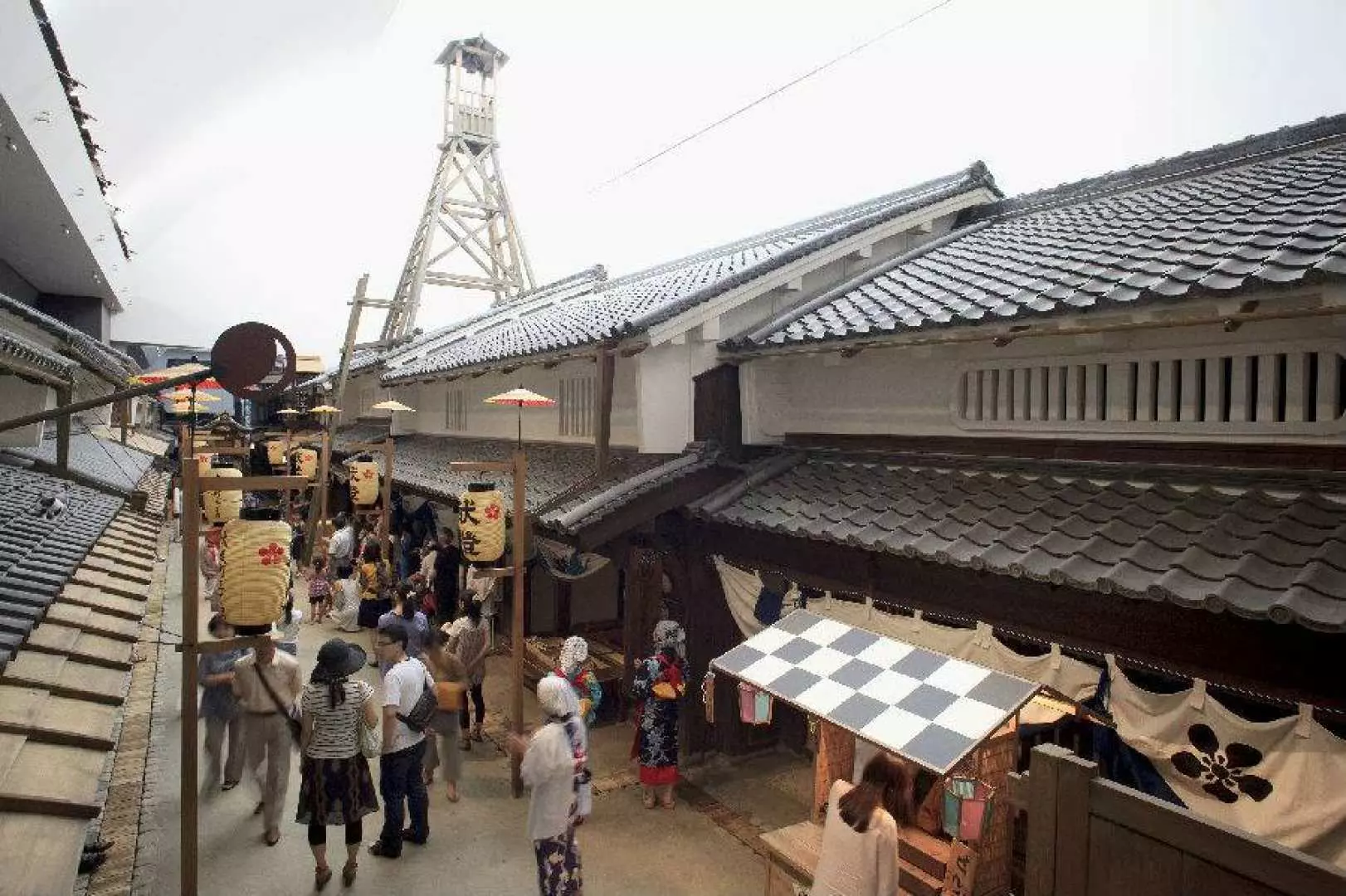 「大阪今昔生活館」內重現的江戶時代繁忙街景，遊客穿梭於瓦片屋頂的傳統日式房屋間，背景高聳的望樓增添歷史氛圍，提供沉浸式體驗。