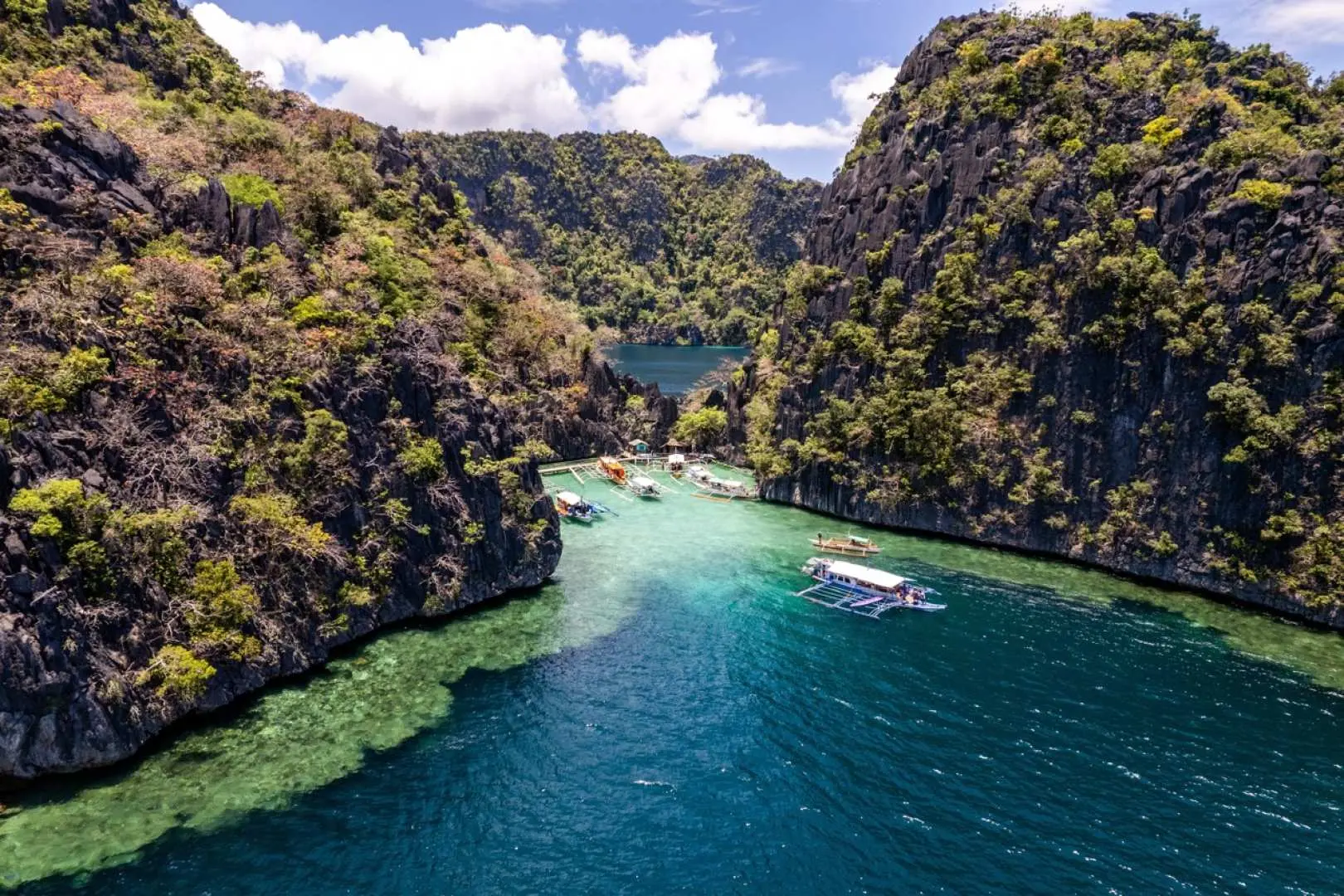 Magnificent Twin Lagoon landscape in Coron, featuring deep blue and turquoise waters flowing between towering limestone cliffs, surrounded by lush vegetation, with a few boats dotting the scene, an ideal spot for exploring natural wonders.