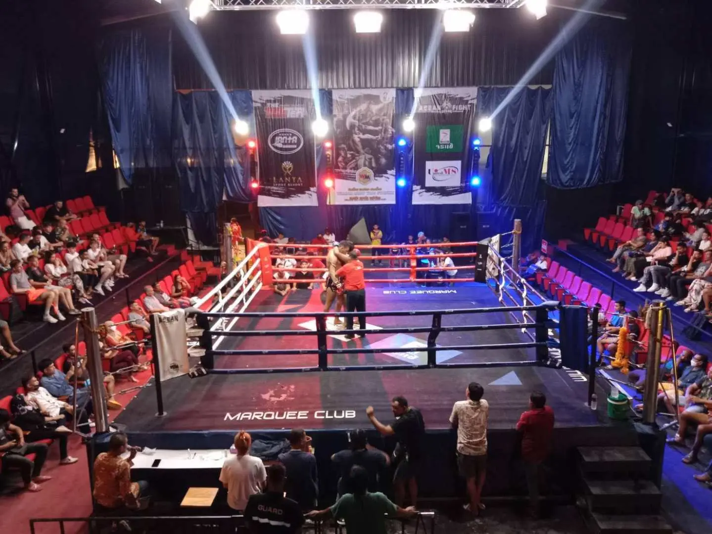 Panoramic view of the Ao Nang Krabi Muay Thai stadium, showcasing the brightly lit boxing ring surrounded by an audience, ready for an exciting live performance.