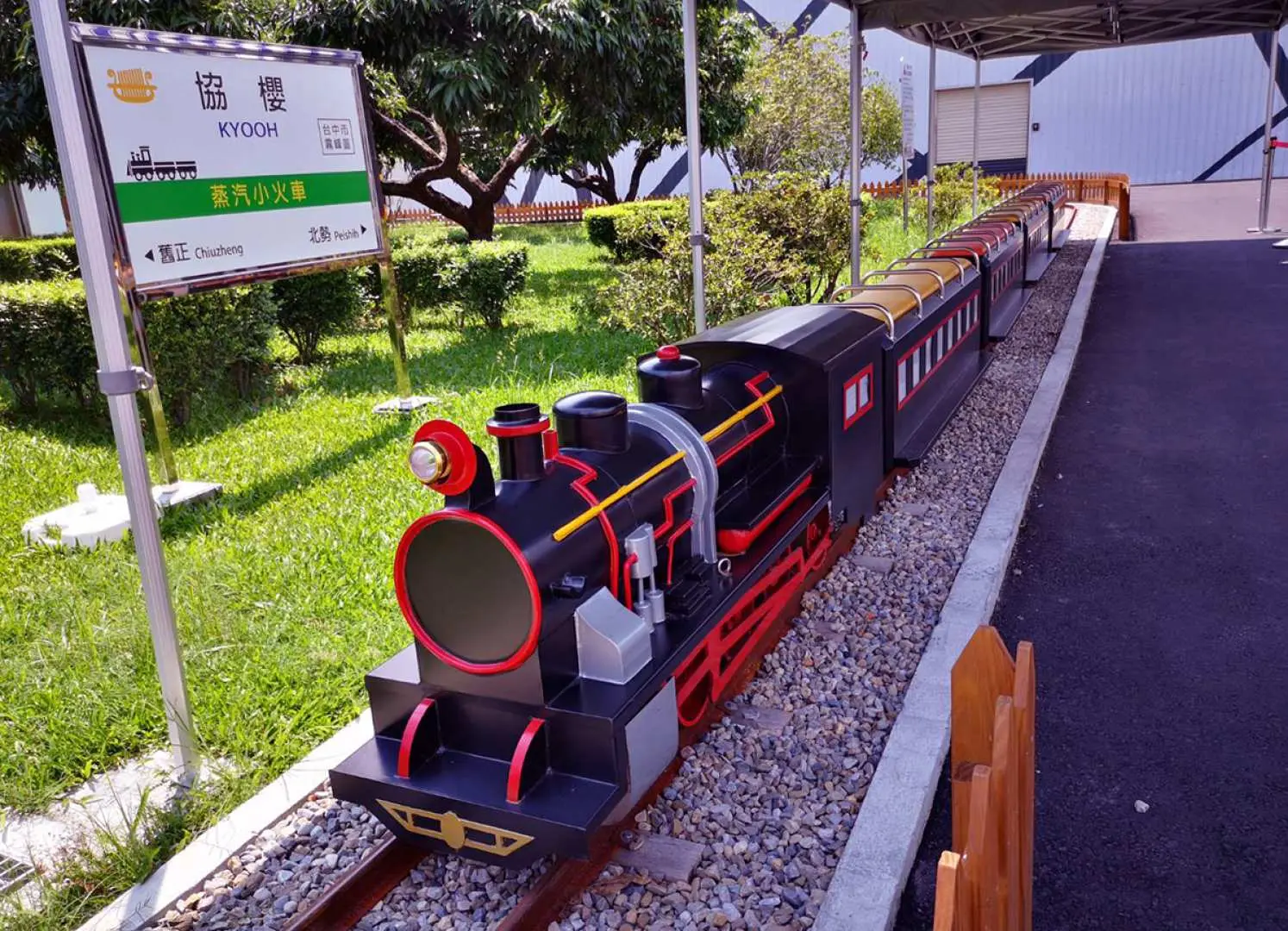 The miniature black and red steam train with passenger cars on tracks at Taiwan Modern Music Boxes Museum, an outdoor recreational attraction popular with families.