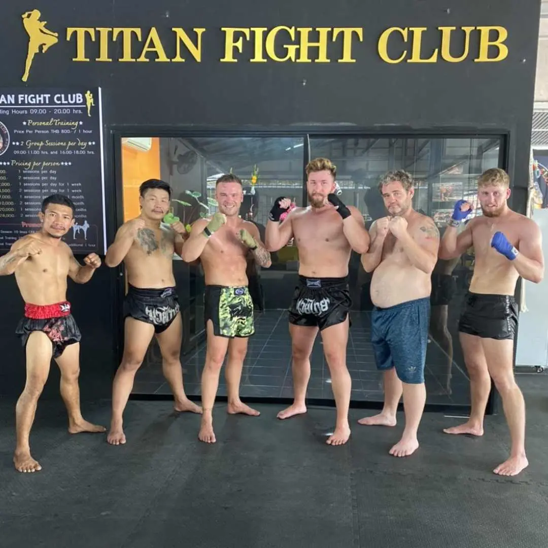 普吉島芭東泰拳訓練館裡，一群男學員與教練們在「Titan Fight Club」標誌前合影，展現泰拳團隊的活力。