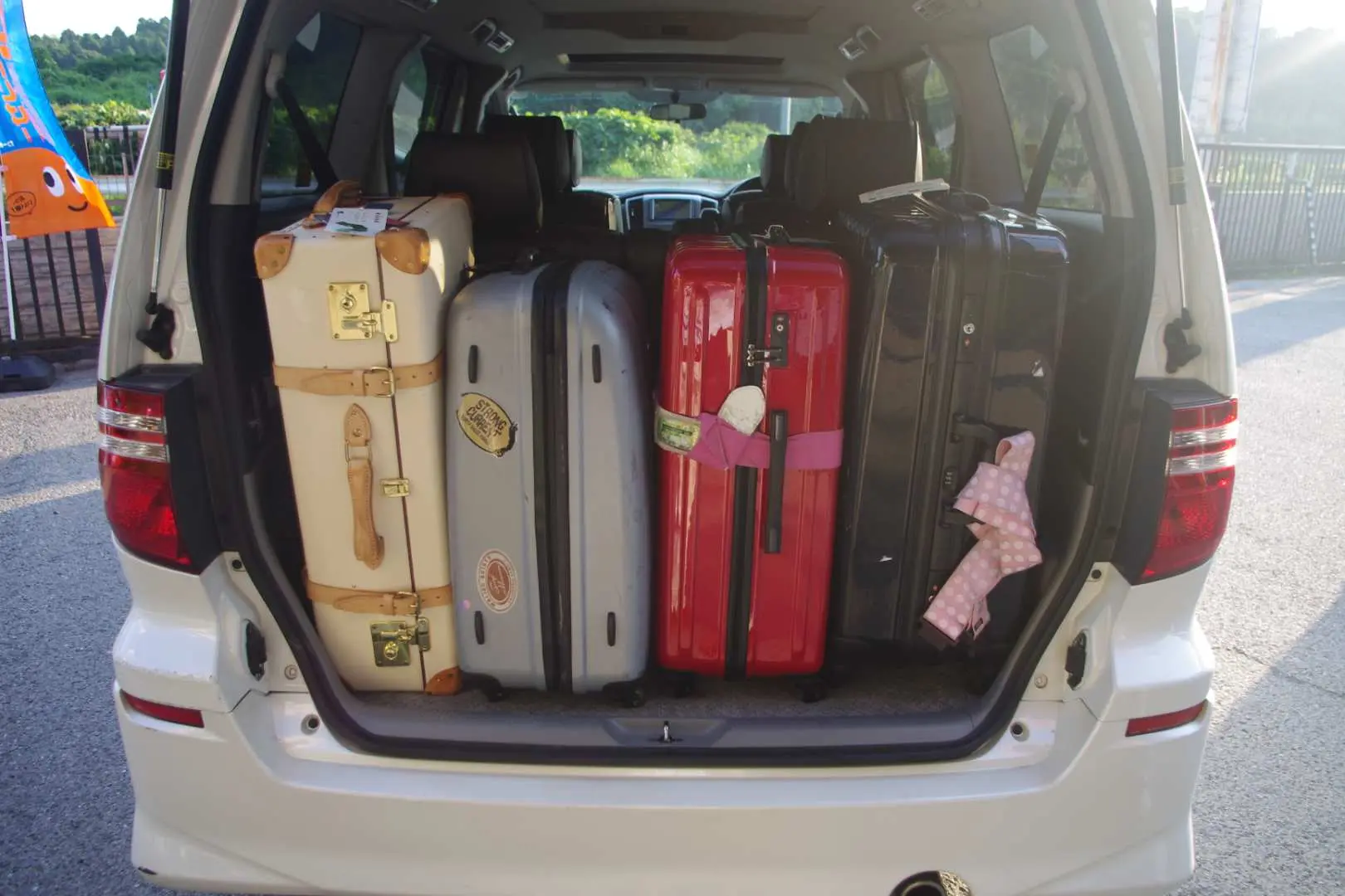 The spacious open trunk of a white minivan filled with multiple large suitcases, offering ample luggage space for families or groups using Okinawa airport transfers.