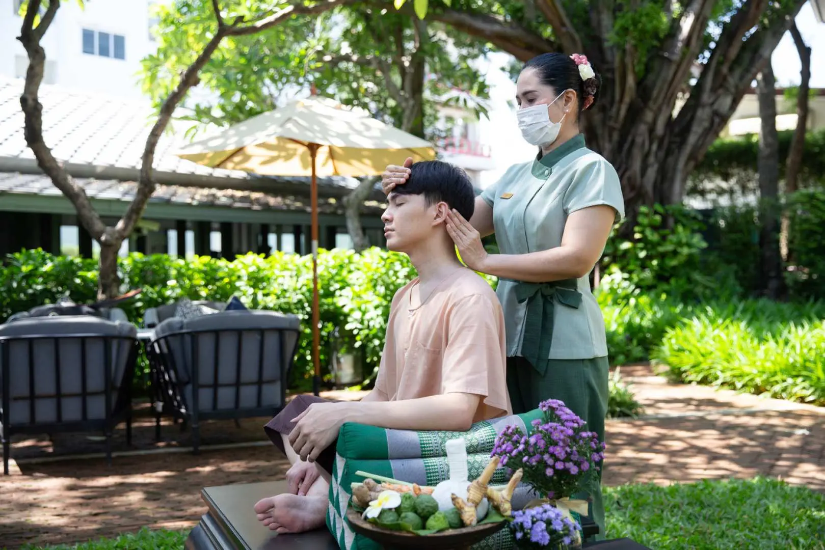 Bangkok Raweekanlaya tropical garden: a male client enjoys an outdoor head, shoulder, and neck massage, experiencing tranquil rejuvenation under nature's canopy.