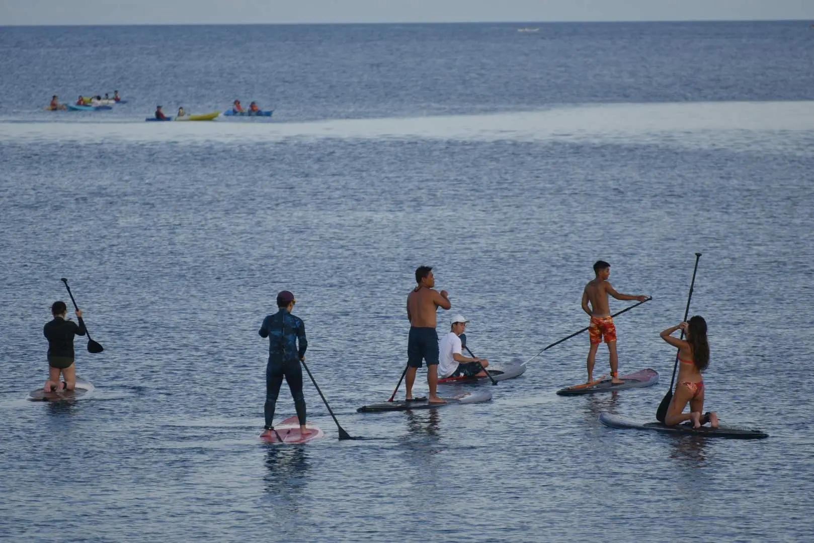 During the Xiaoliuqiu Bear Dive SUP stand-up paddleboard experience in Taiwan, multiple participants are standing or kneeling on paddleboards in the azure ocean, enjoying diverse water sports, with other boats visible in the distance.