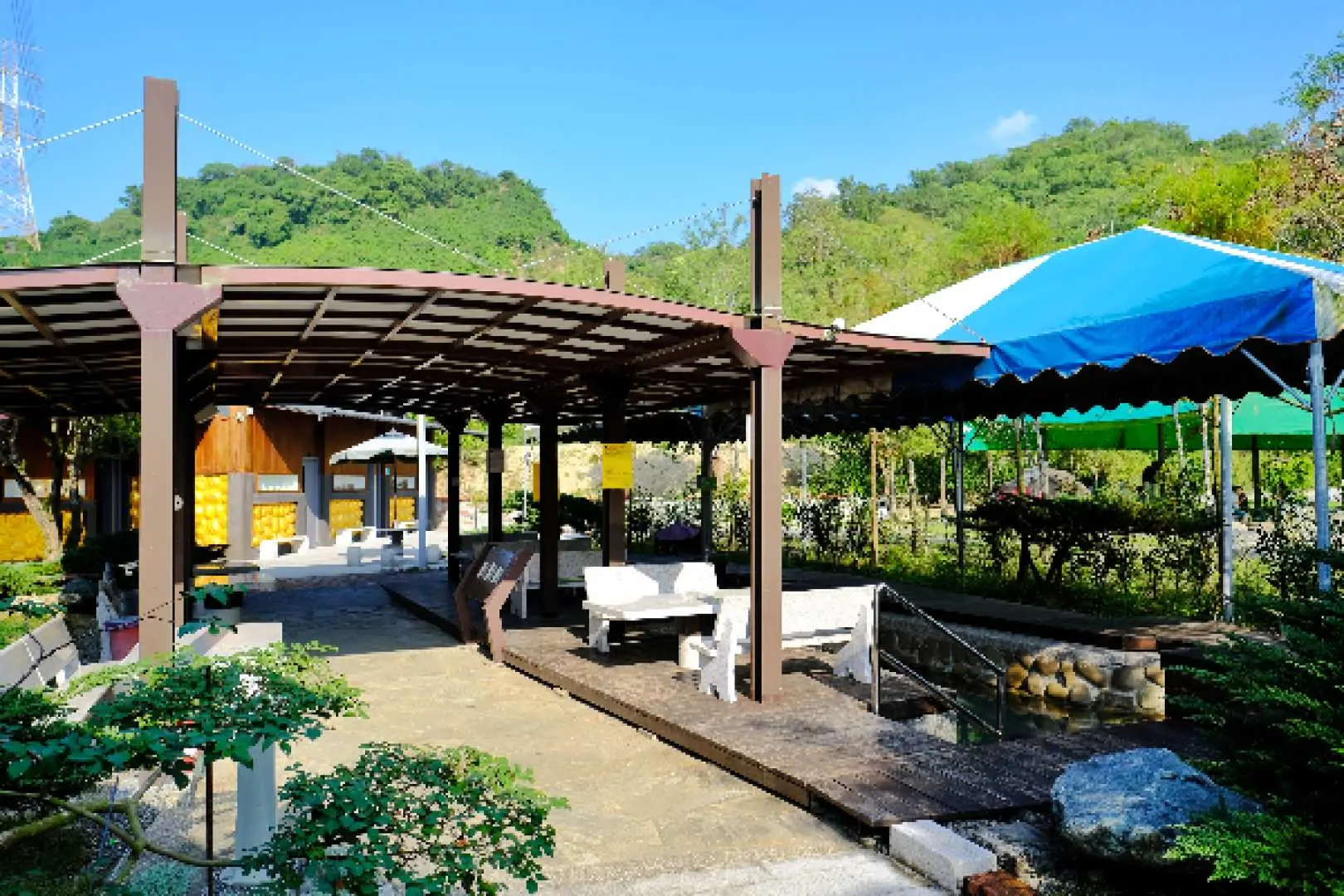 沐浴在陽光下的台南龜丹溫泉戶外包池區，遠處青山連綿，每個獨立湯池區皆有遮棚與桌椅，營造舒適的度假氛圍。