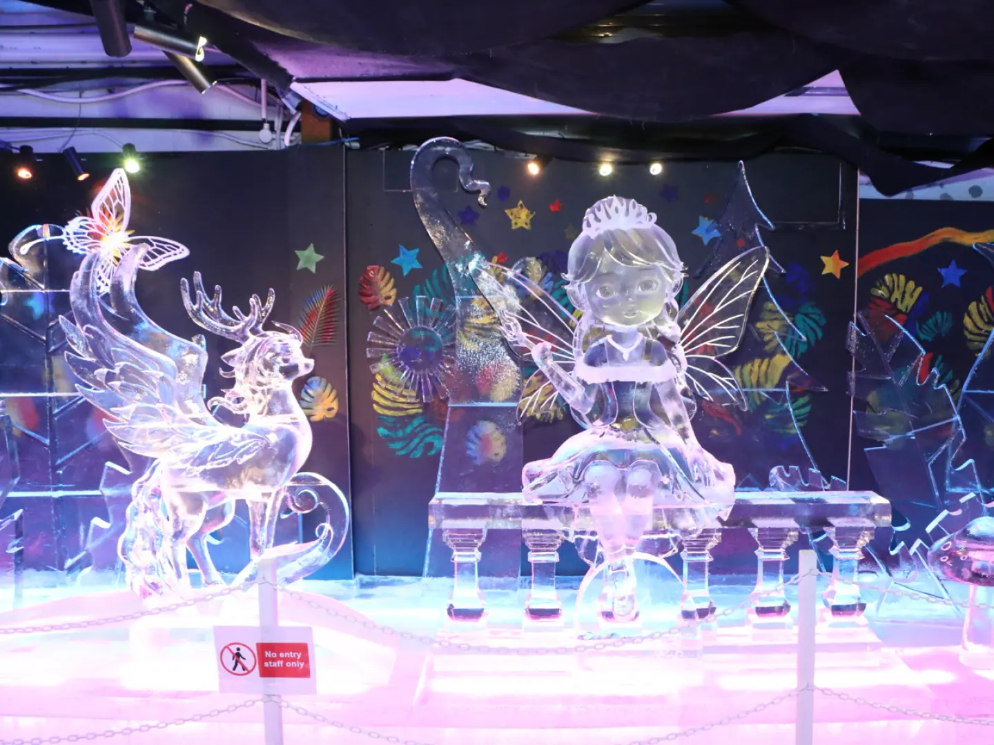 Exquisite ice sculptures of a fantasy fairy and a winged deer are displayed within Singapore Snow City, creating a magical ice wonderland under colorful lights.