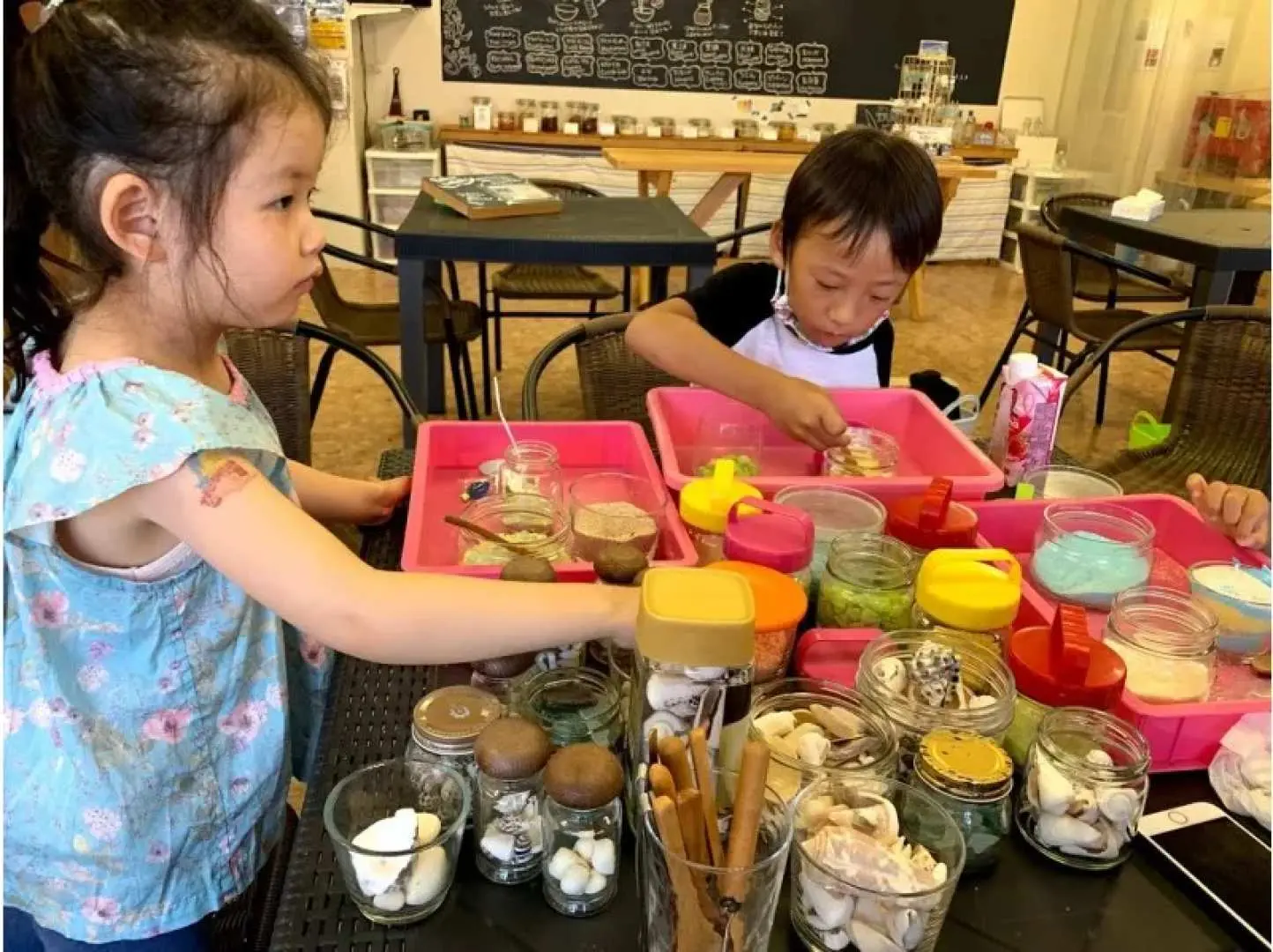 Two children engaged in the Ishigaki Island transparent candle making experience, selecting and arranging shells, sand, and marine elements.