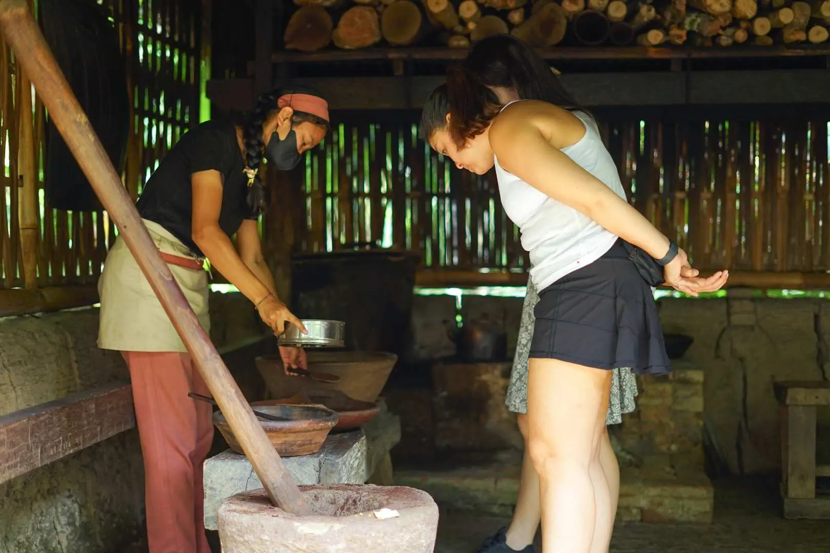A tourist observes a local guide demonstrating the traditional hand-pounding method for processing coffee beans, highlighting the artisanal craft at Bali Pulina.