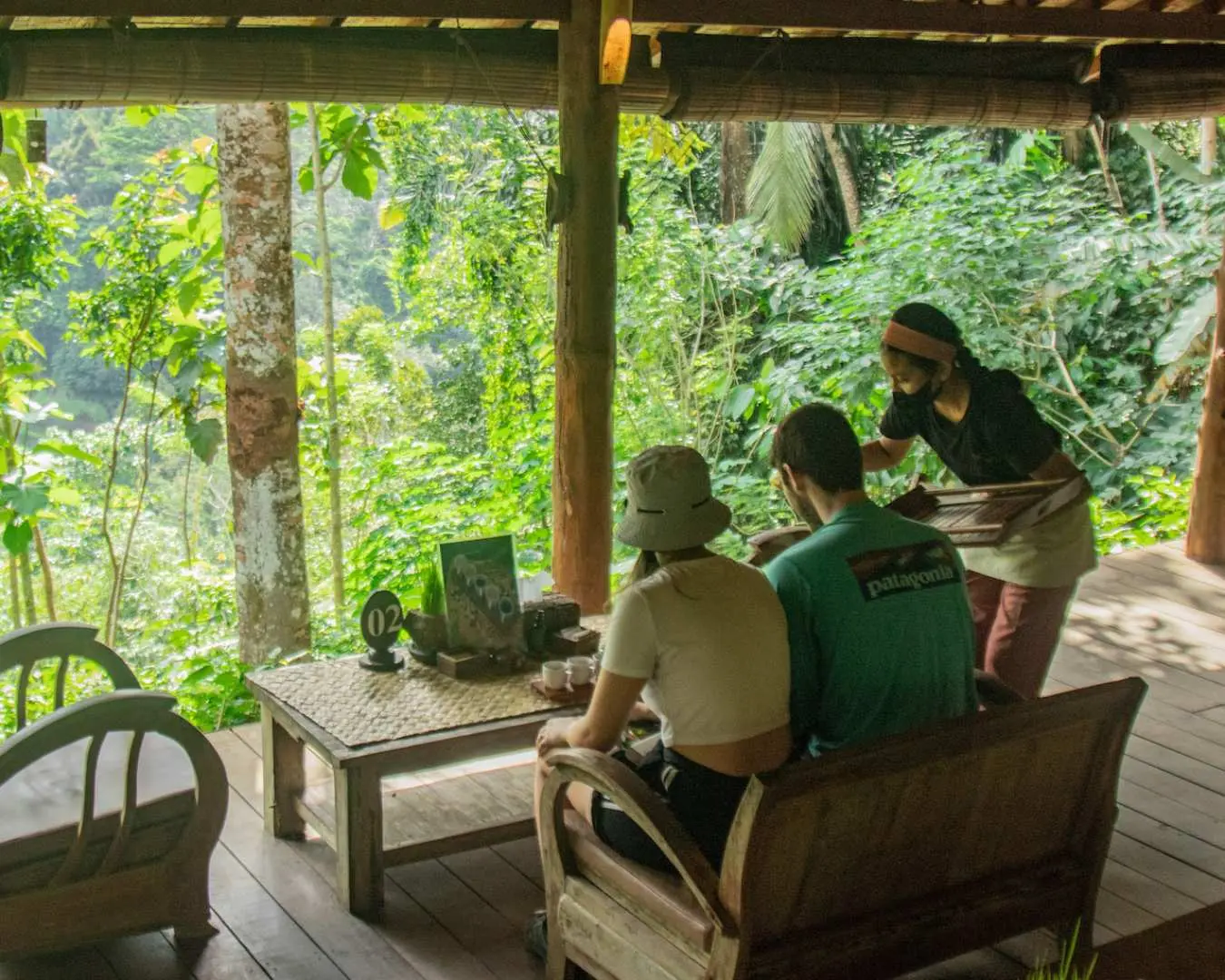 Visitors relax on a scenic outdoor deck at Bali Pulina, enjoying their coffee amidst the breathtaking tropical rainforest views, immersing in Bali's natural beauty.