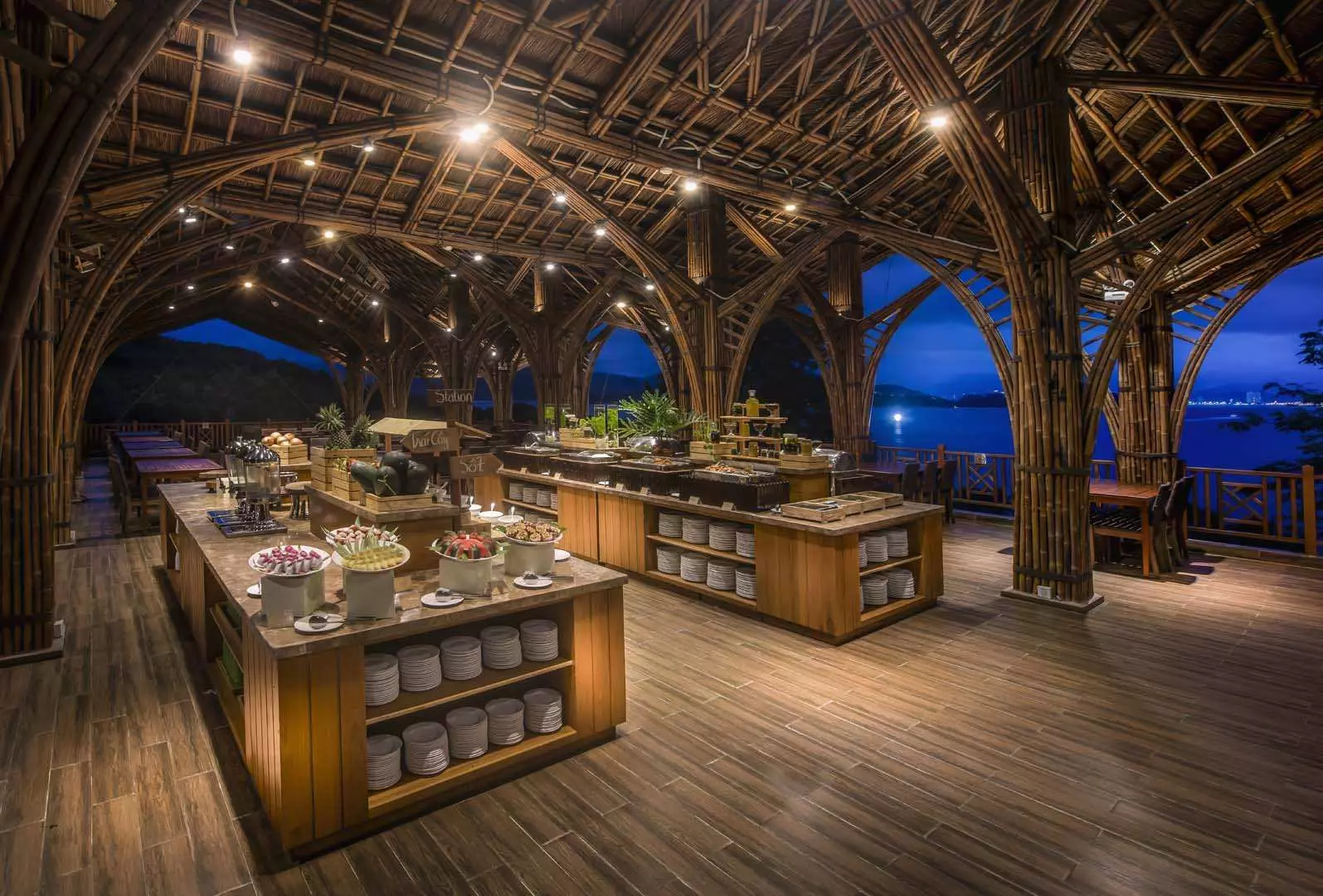 Night view of Soul Viet Restaurant at Hon Tam Island, Nha Trang, with unique bamboo arched ceilings glowing under warm lighting, a ready buffet area, and beautiful bay views.